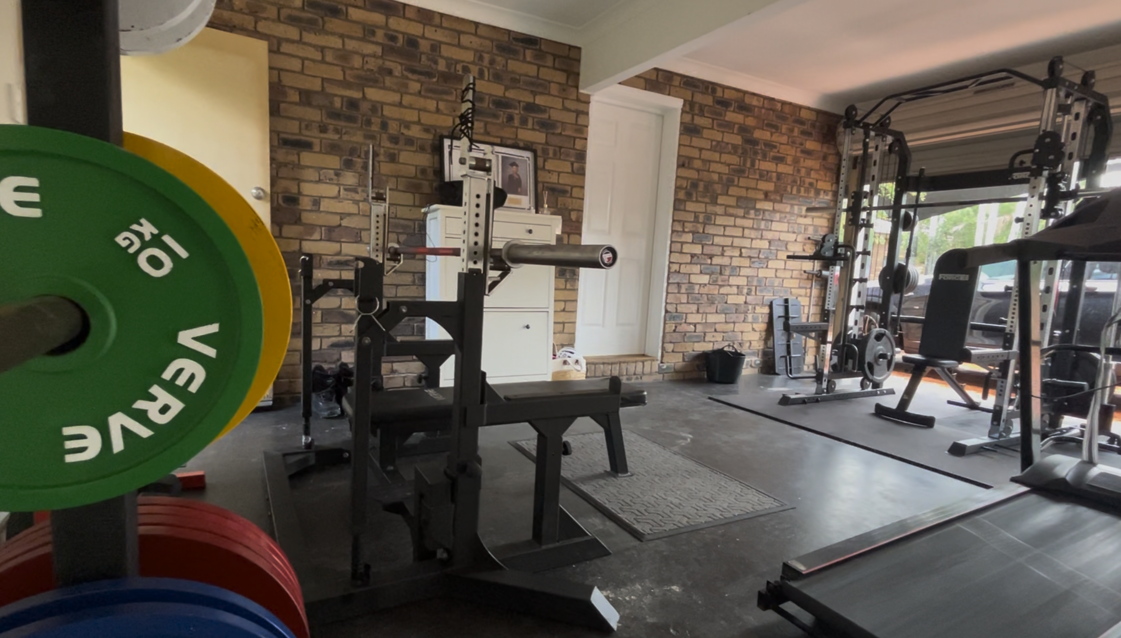 Inside the home garage gym at Stampede Performance Sunnybank / Robertson. Fully equipped with combo rack, calibrated plates, treadmill, deadlift platform and bar, and cable station.