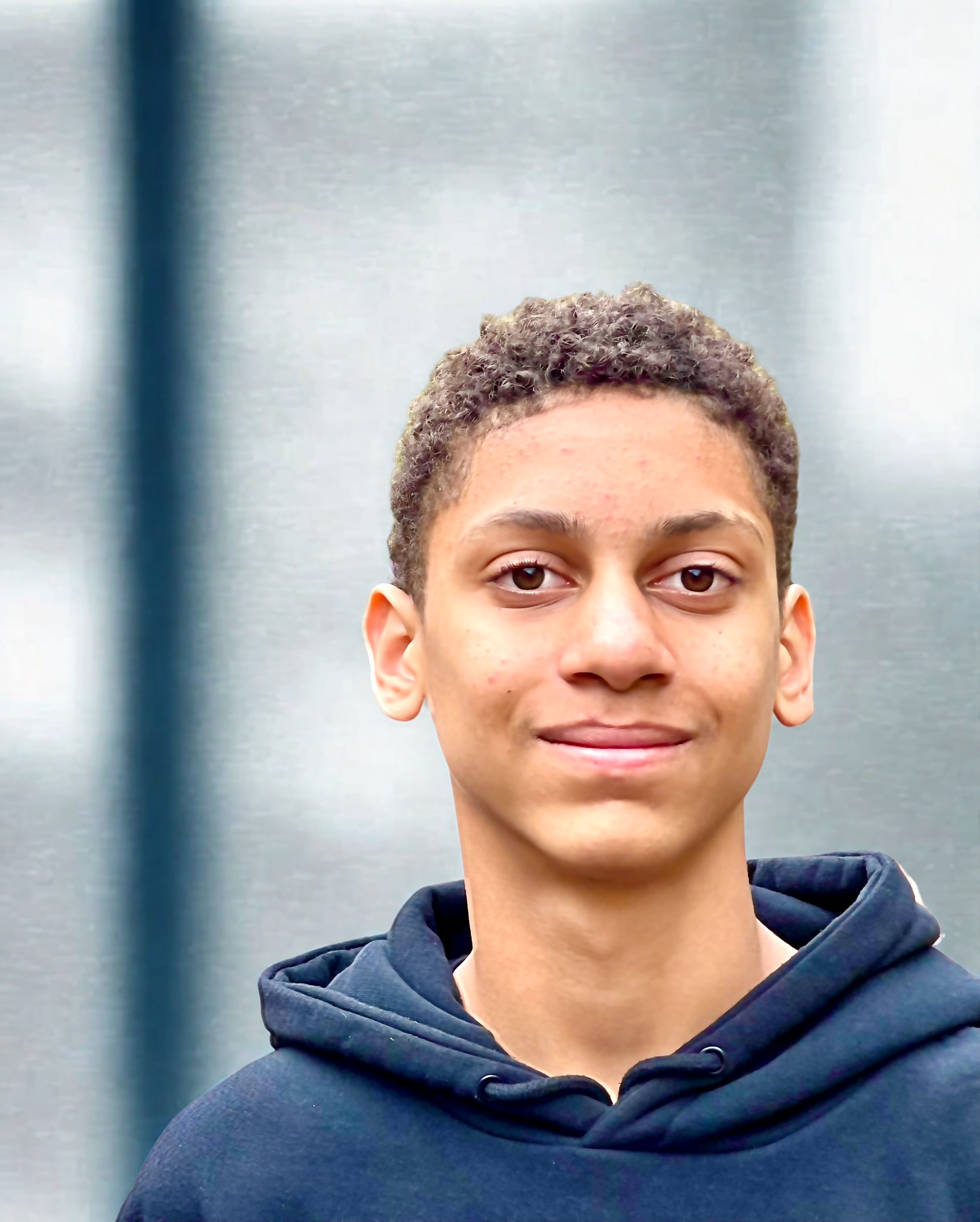 Close-up of a young man's face with curly hair, wearing a hoodie, in an indoor setting.