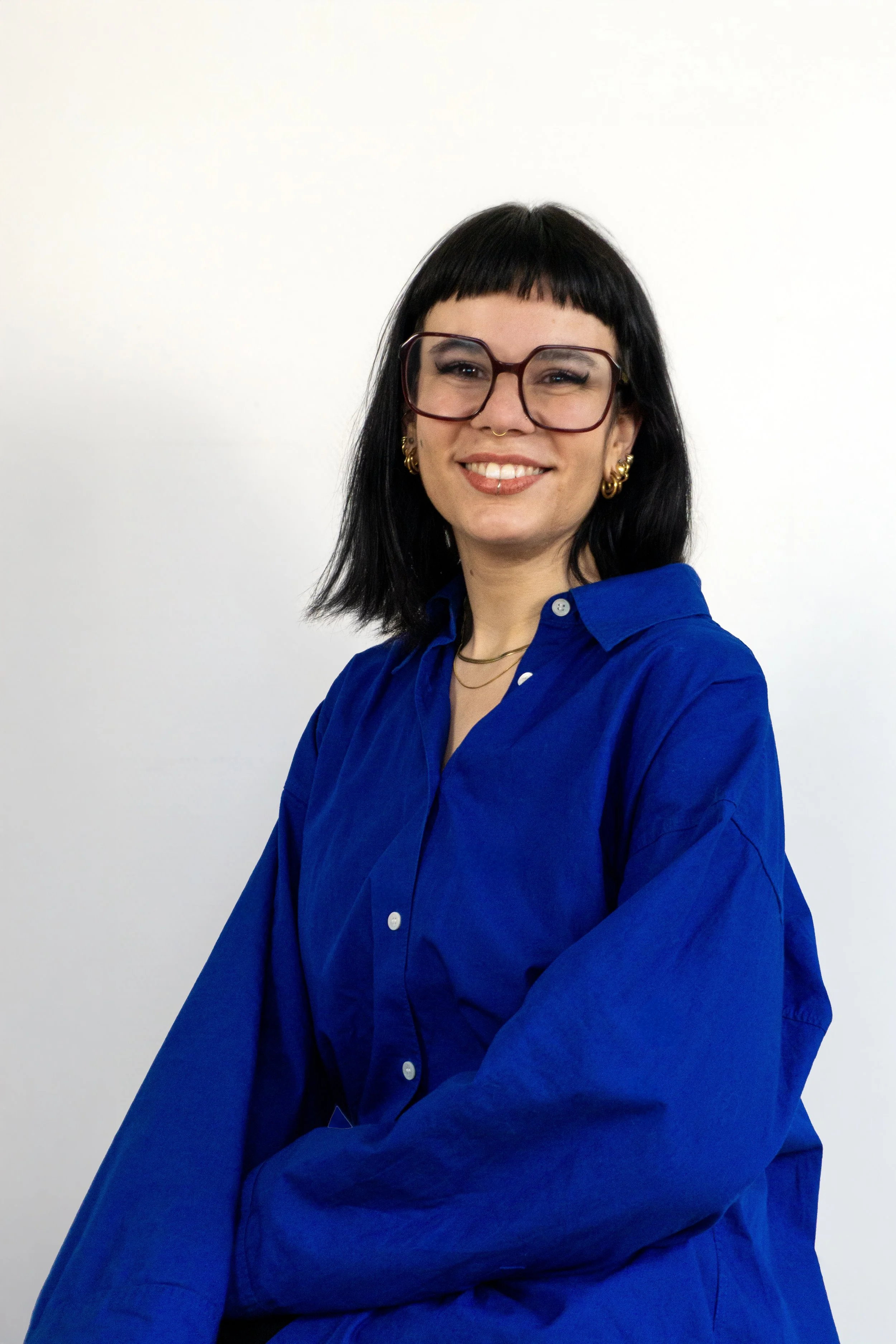 Portrait von Hebamme Jacky, sie trägt ein blaues Hemd, hat eine Brille und schwarze Haare