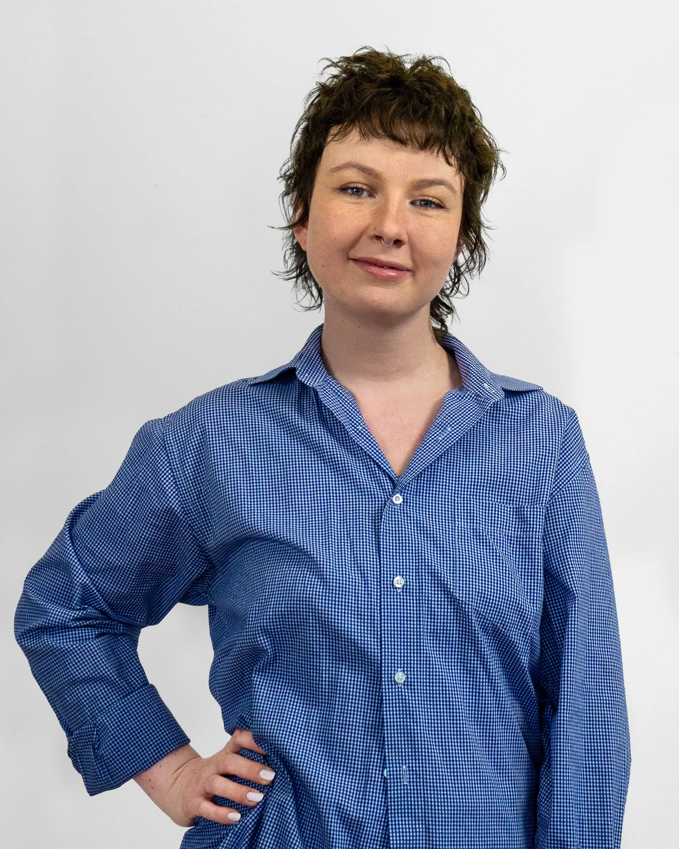 Portrait von Hebamme Laura, sie hat kurze lockige Haare, trägt ein blau kariertes Hemd