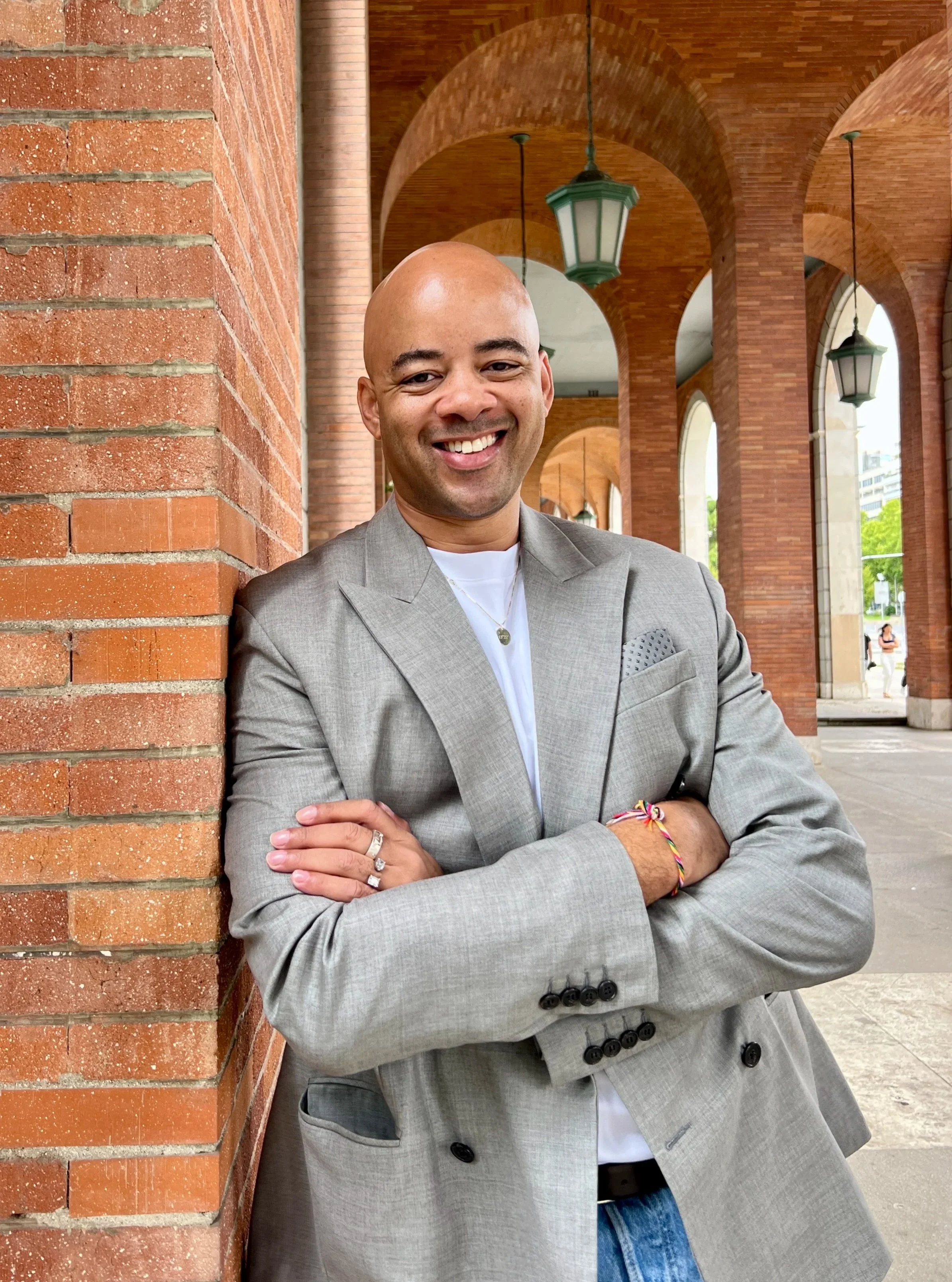 Photo of Ethan Ward, founder of HEATDRAWN Media, in a gray double-breasted jacket, leaning against a brick column