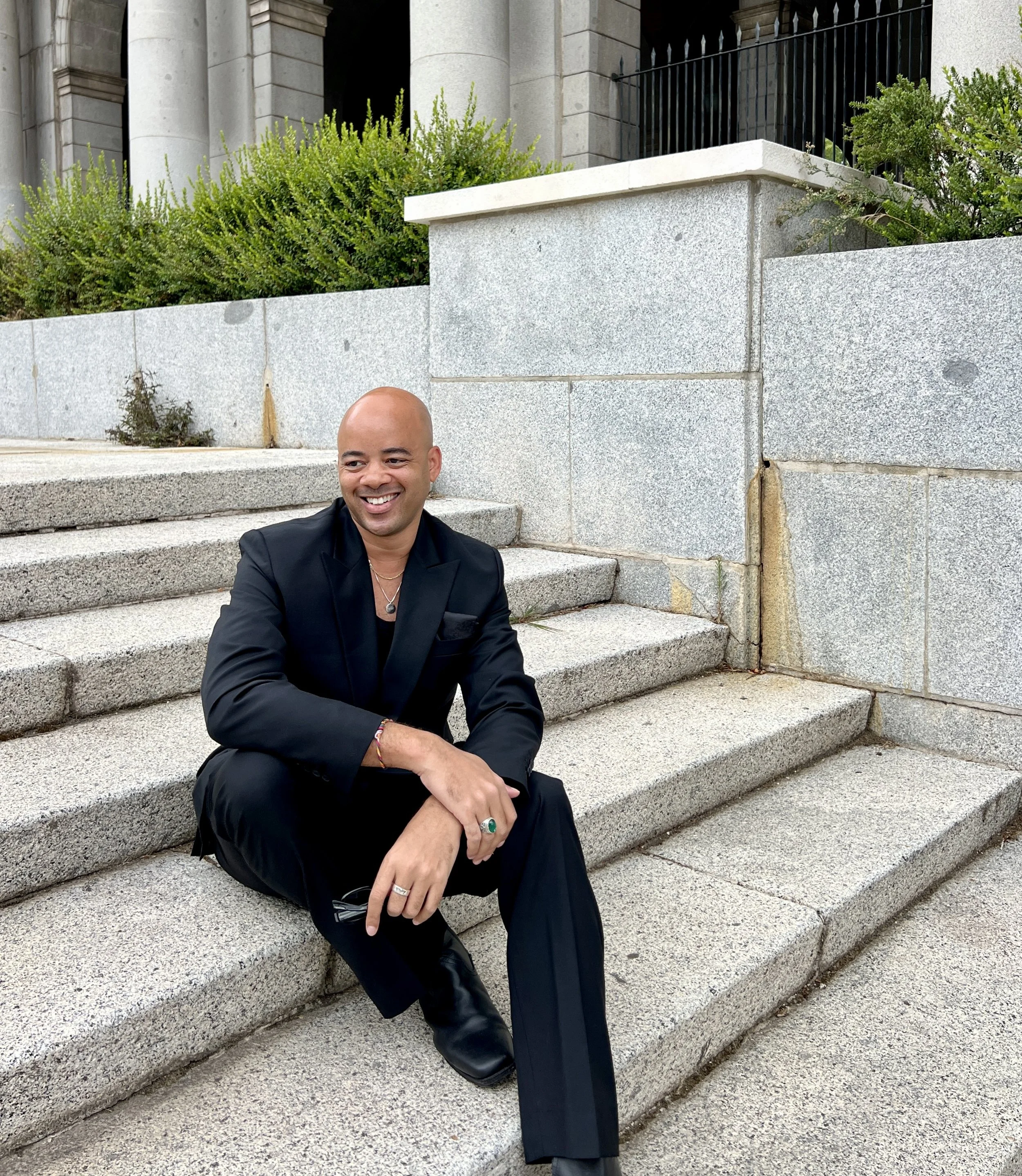 Photo of Ethan Ward in a black suit, sitting on stone steps and smiling