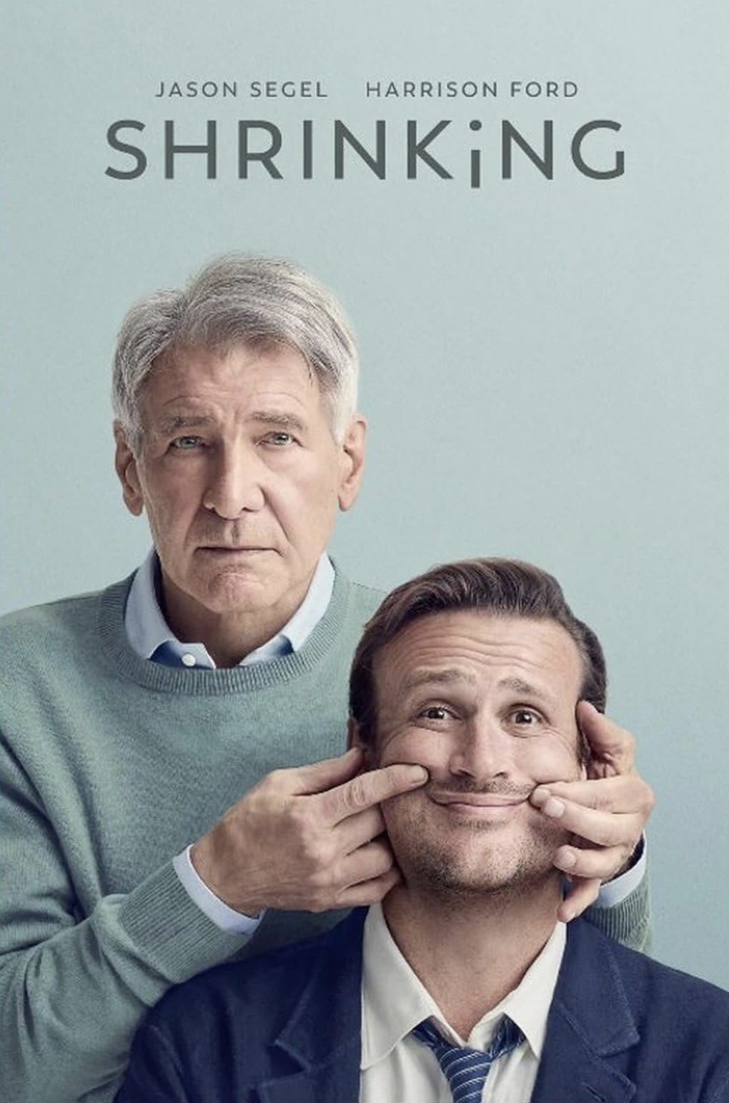 The cover of the book titled 'Shrinking' features two men. The older man with gray hair is behind and has a serious expression. The younger man with dark hair is smiling while being playfully manipulated by the older man, who is stretching his cheeks