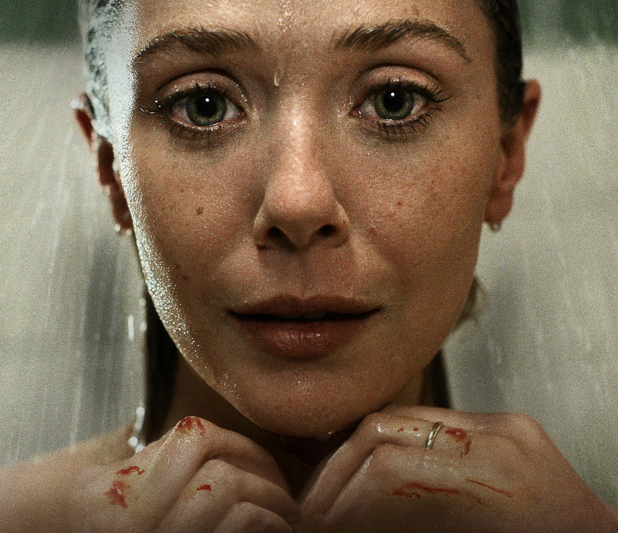 A close-up of a woman with wet hair, looking directly at the camera with her hands near her chin, with some blood on her fingers.