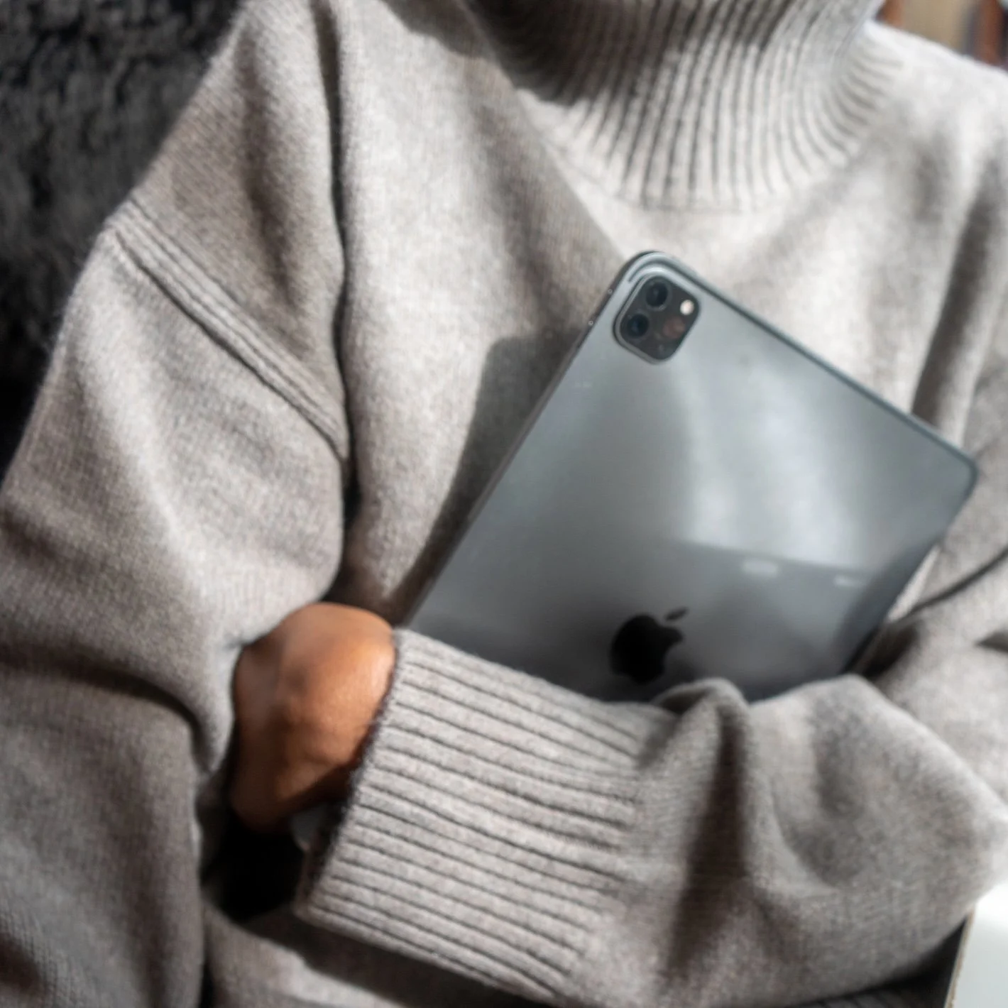 Person wearing a beige sweater holding a silver iPhone in front of their chest.