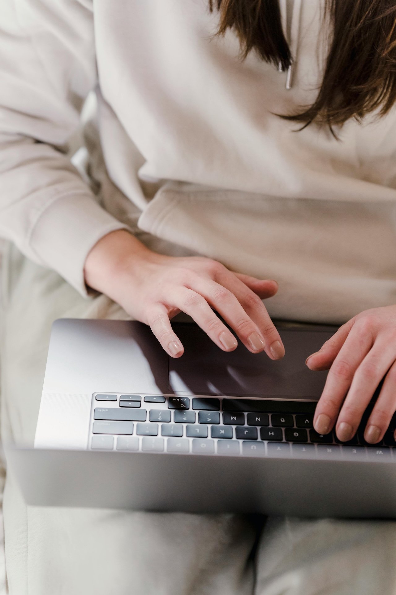 Person working on a laptop, wearing a beige sweatshirt.