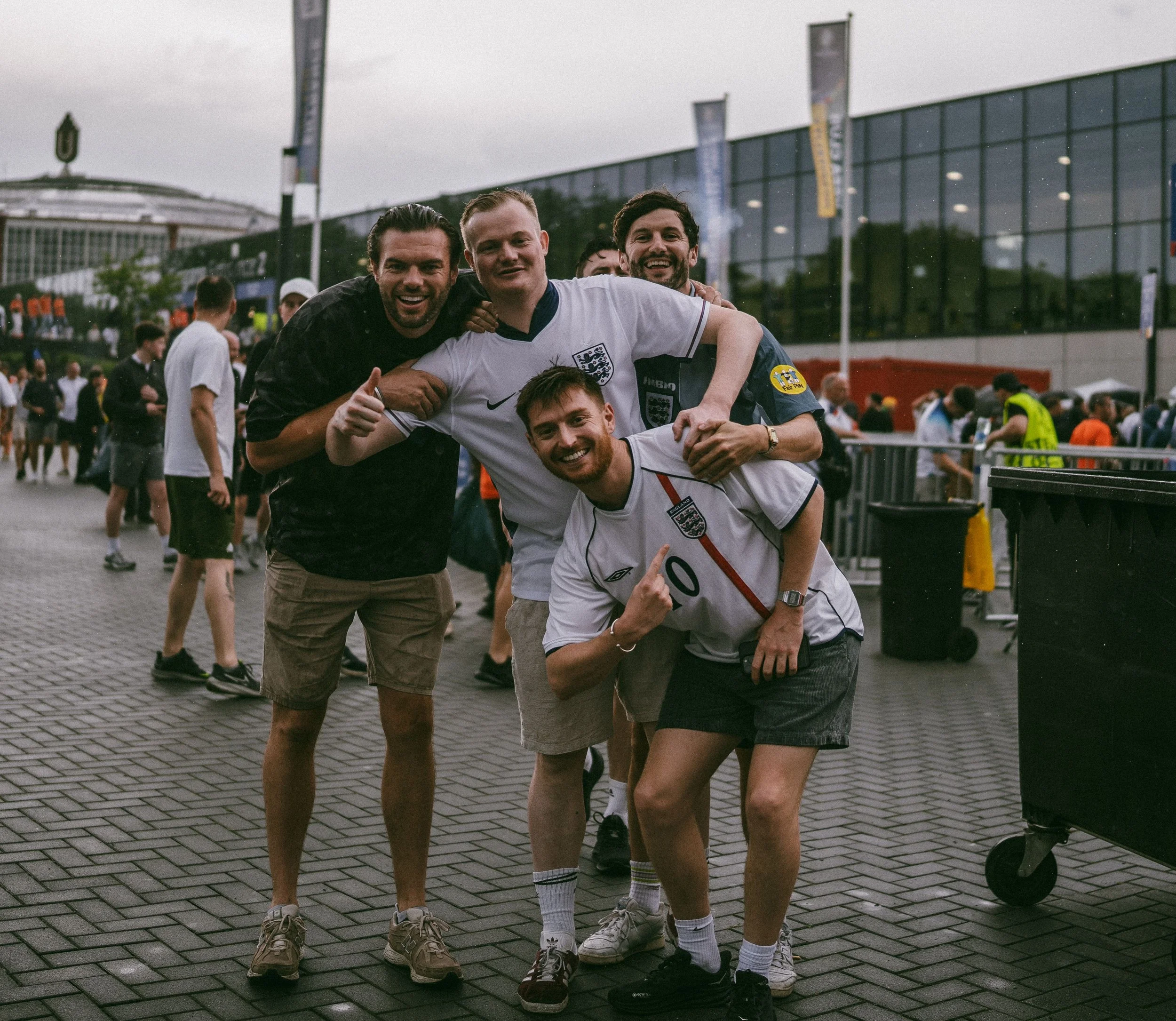 Group of young men smiling and celebrating outdoors after a sports match, with a modern glass building and other people in the background.