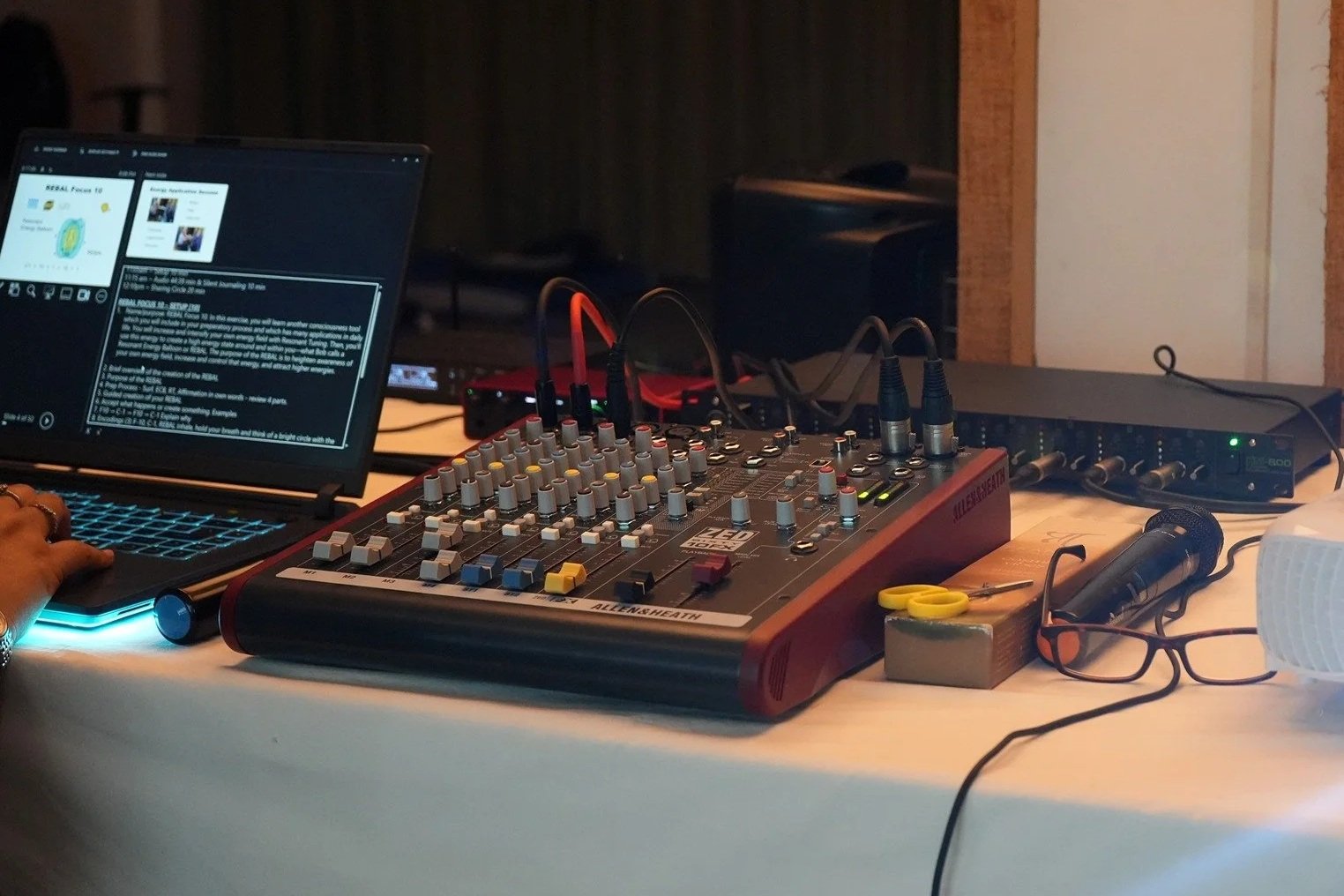 Monre Institute training setup - Mixing console with knobs and sliders, connected to a laptop showing a presentation or document, on a desk.
