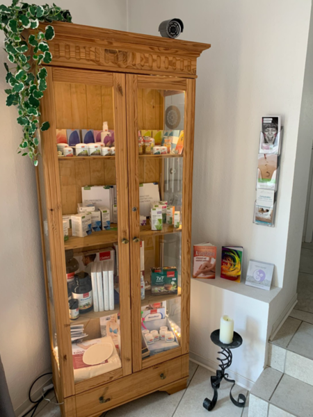 Innenansicht des Wartebereichs der Sanadios Ganzheitliche Naturheilpraxis in Mainz-Hechtsheim mit beleuchtetem Holzschrank und ruhiger Praxisatmosphäre.