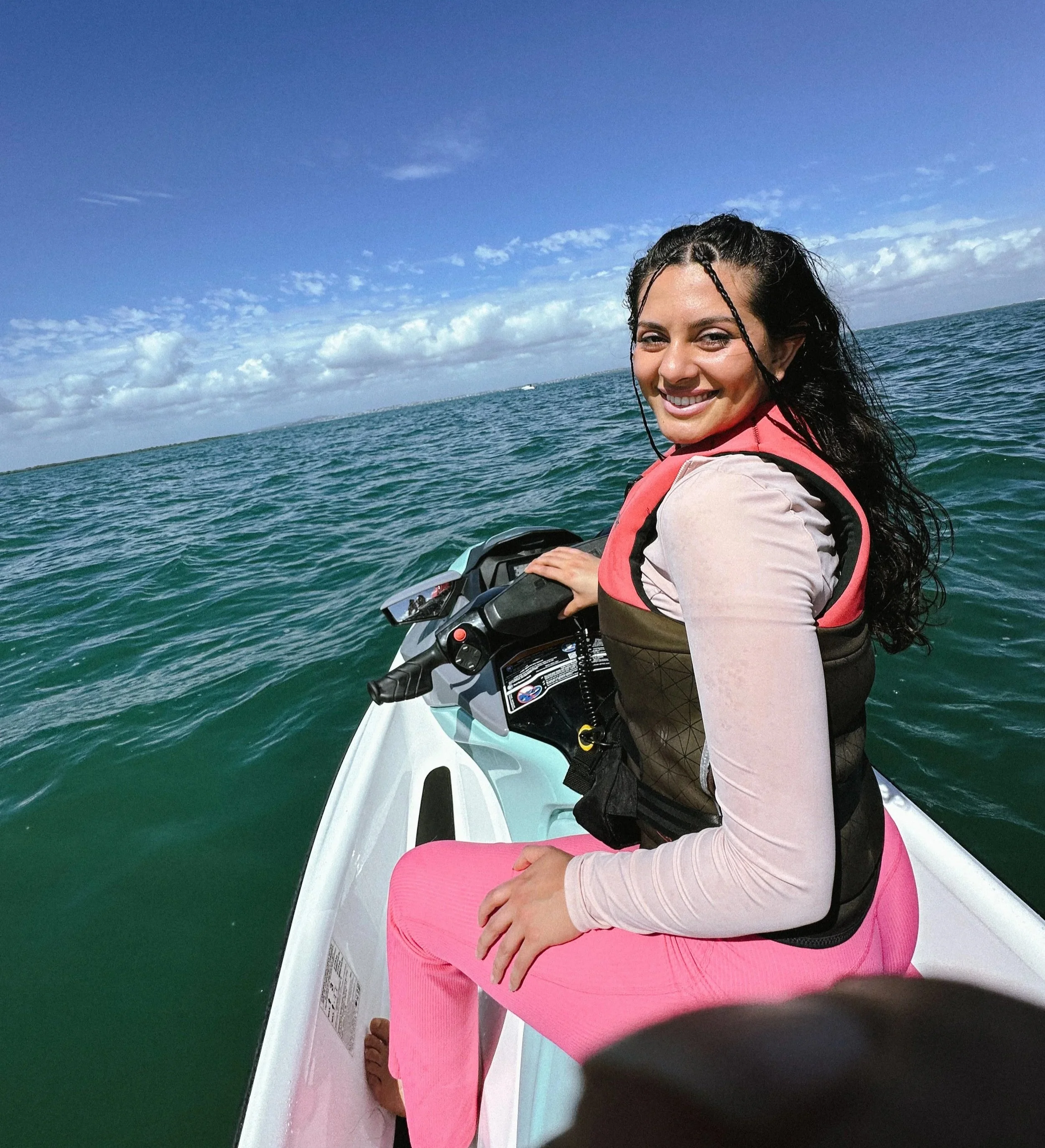 Woman smiling on a jet ski on the water during sunny weather with a blue sky and clouds.