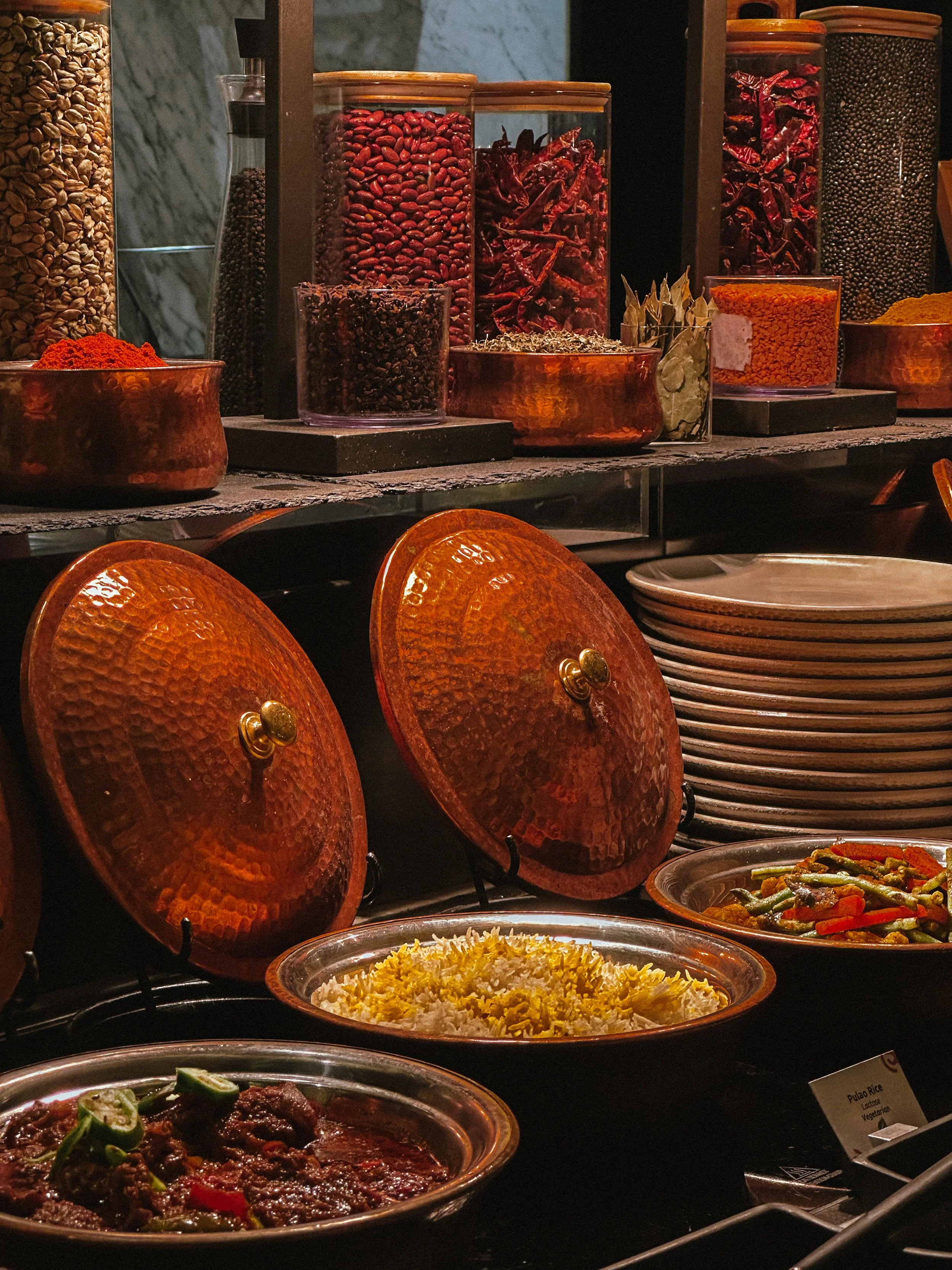 Buffet station with various spices, dishes, and plates of rice, beef stew, and vegetables.