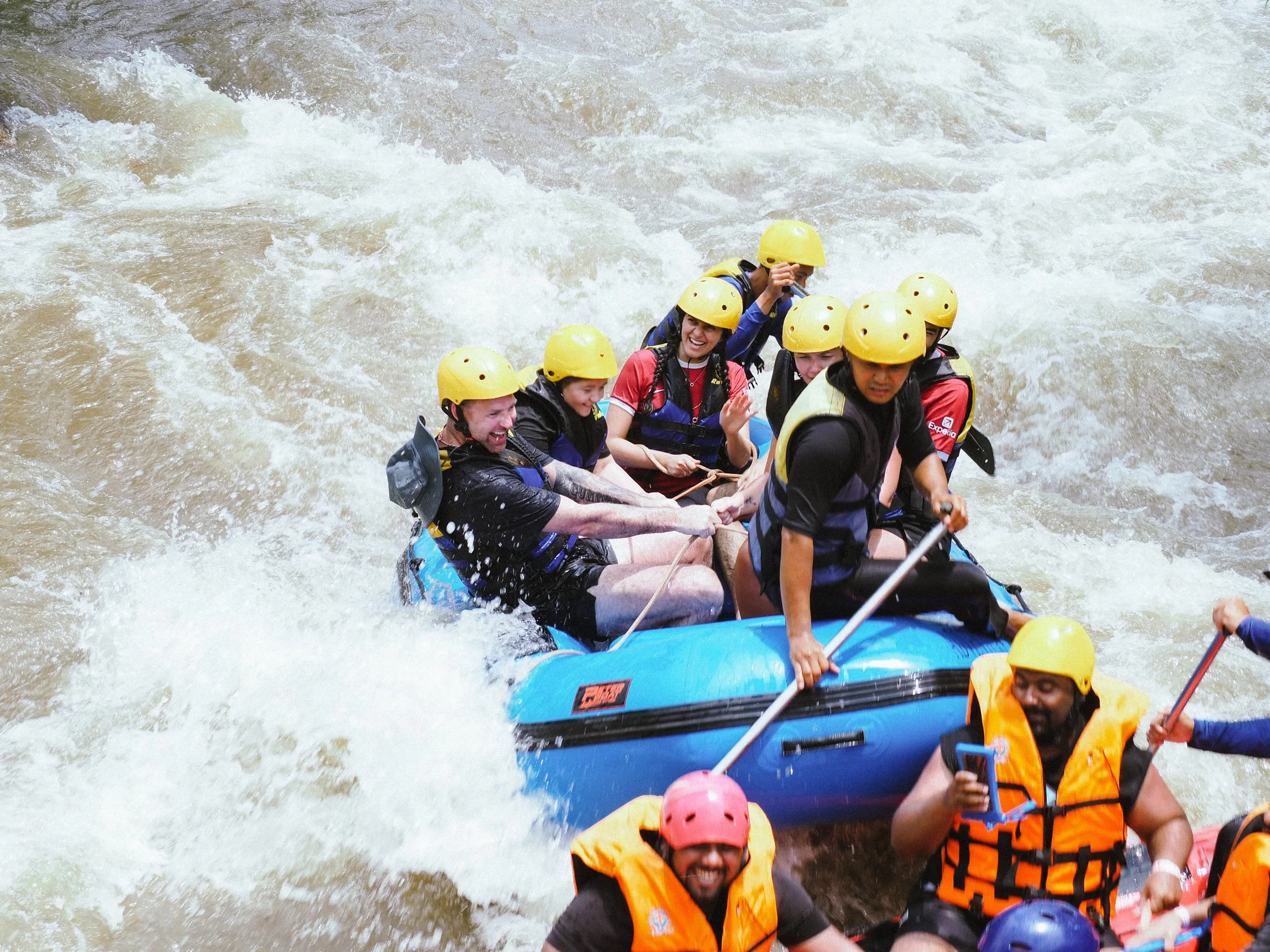 People white-water rafting with yellow helmets and life jackets in river.