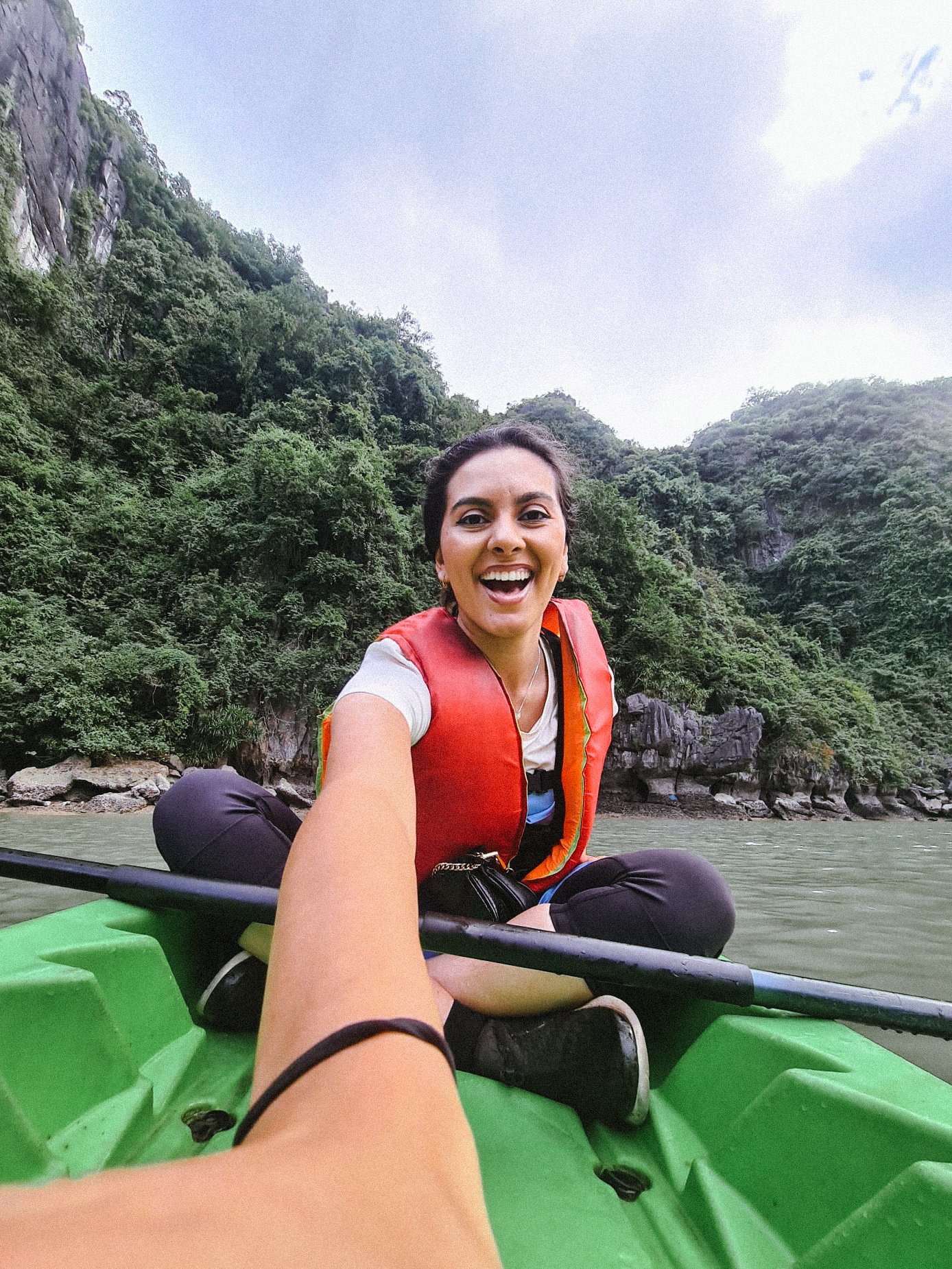 Woman smiling sitting in a green kayak on a river with lush green mountains in the background.