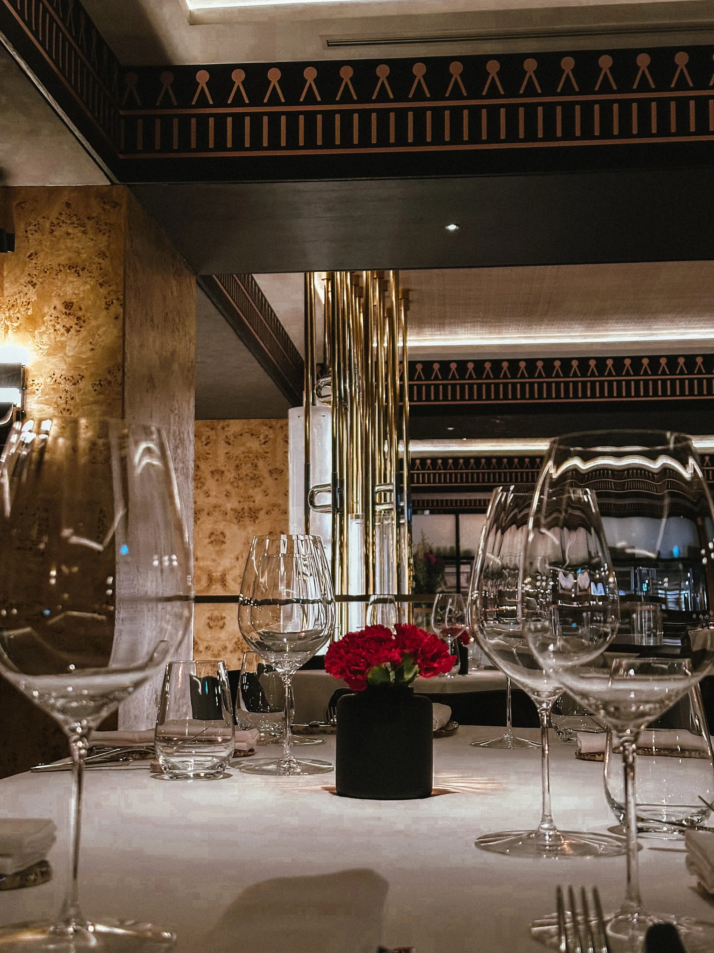Elegant restaurant table setting with glassware and a small red flower arrangement in a black vase.