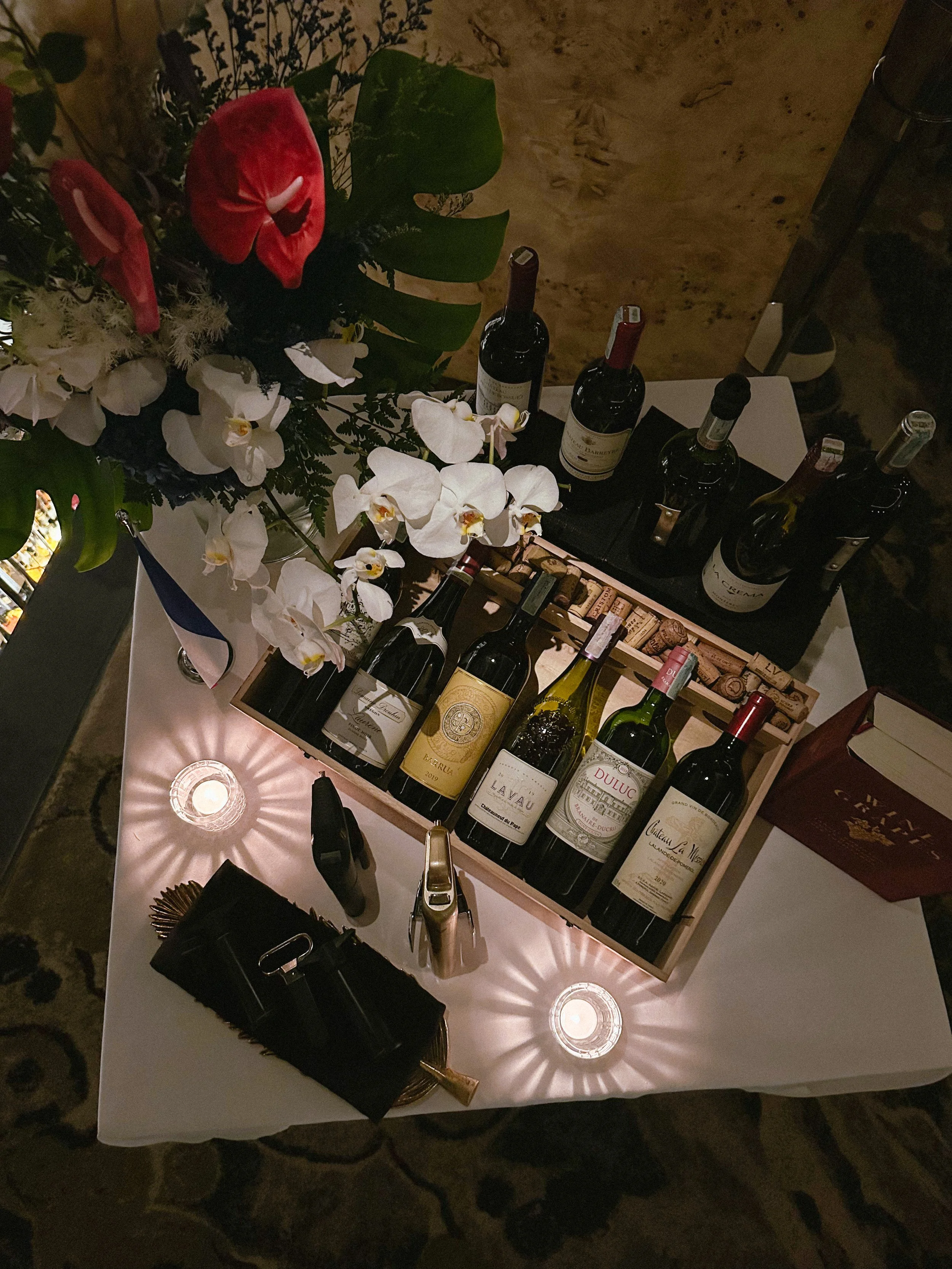 A table with a bouquet of flowers, several bottles of wine, and lights creating a starburst pattern on the tablecloth.