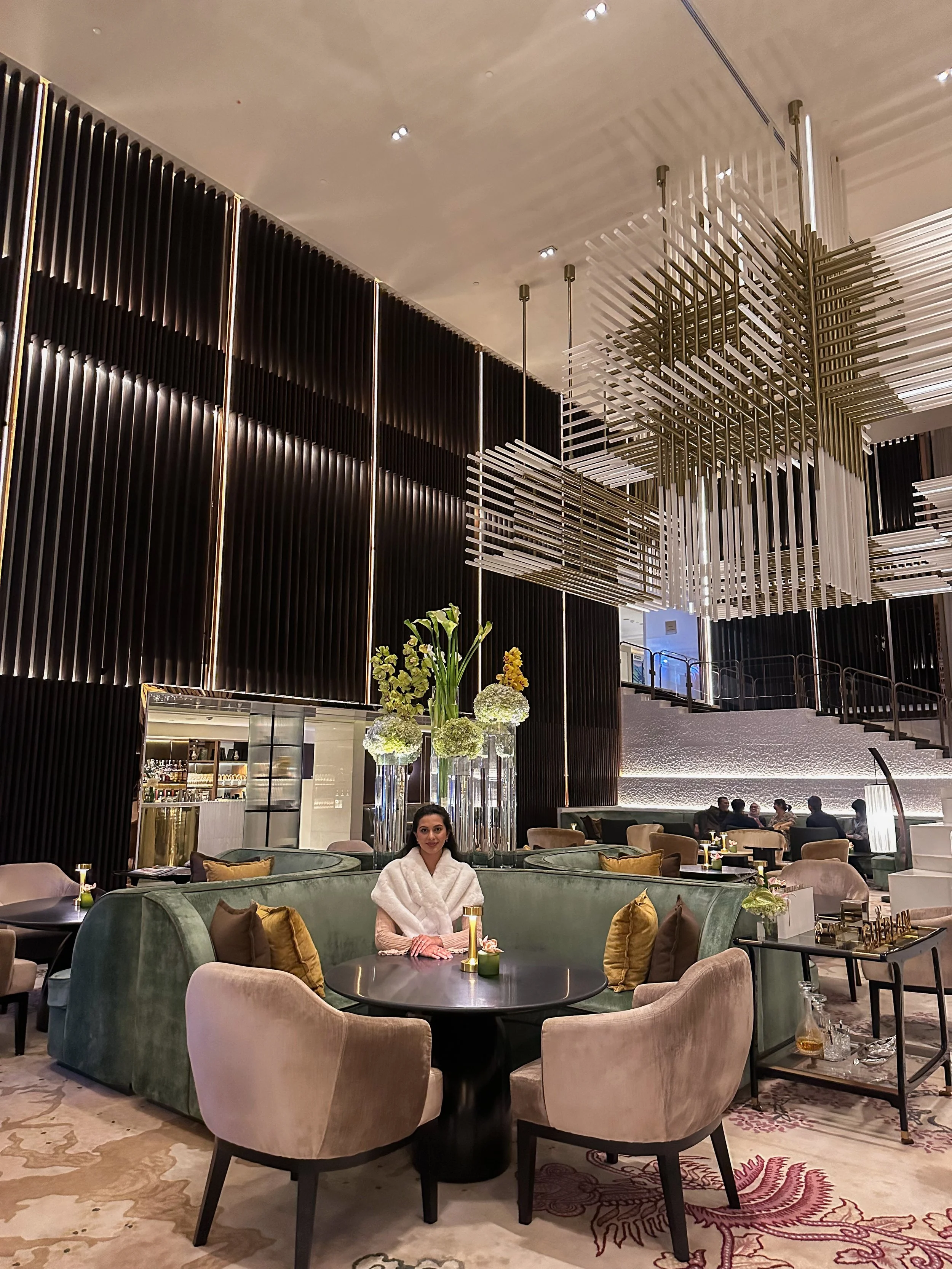 Interior of a modern upscale restaurant or lounge with stylish furniture, large floral arrangements, and a high ceiling with artistic hanging decor.
