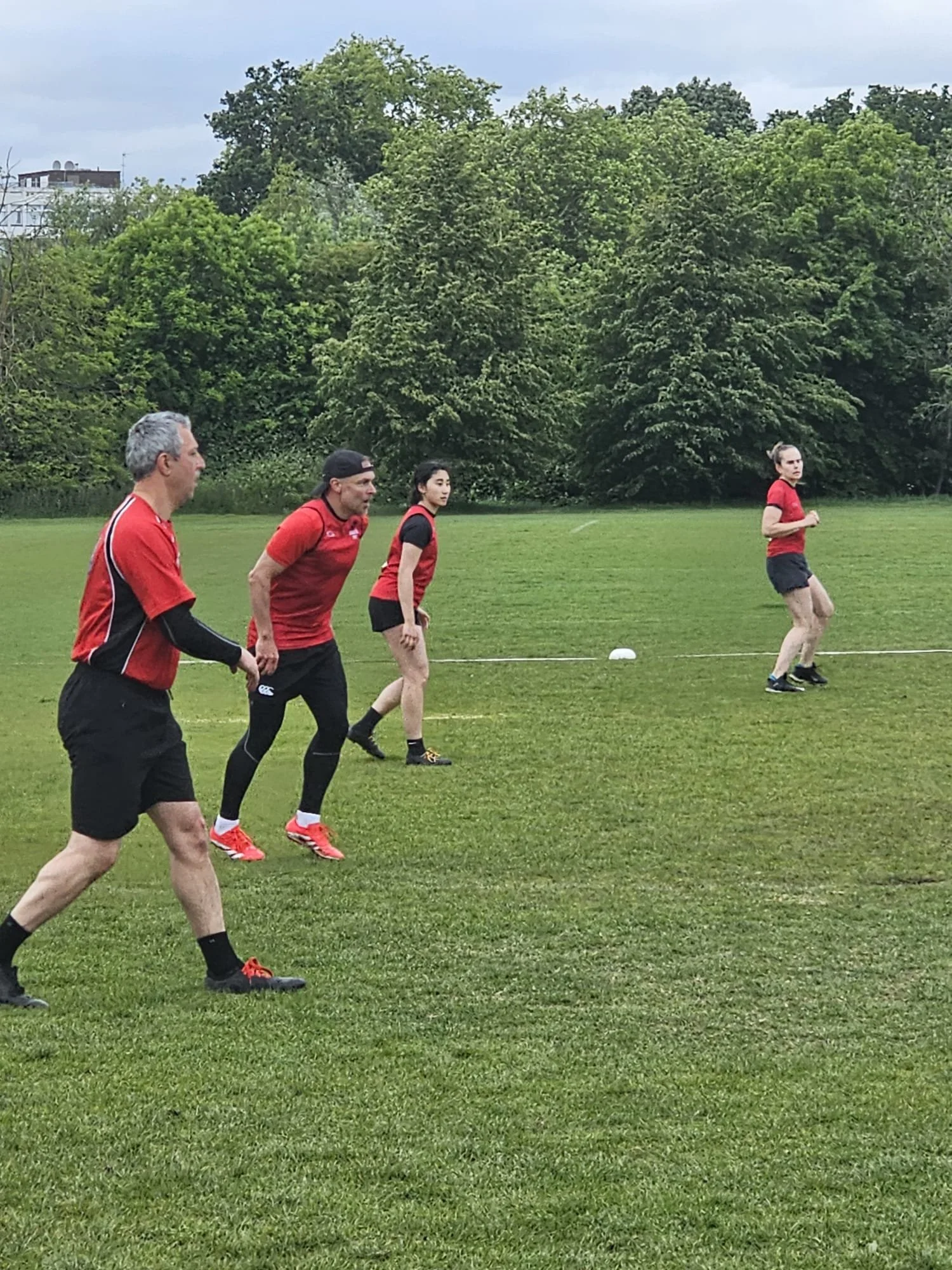 Four people in athletic clothing running or jogging on a grassy field with trees in the background.