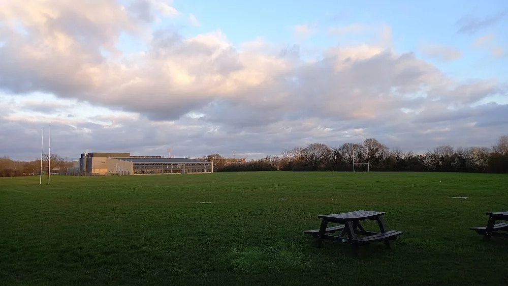 Empty field with picnic table and goalposts, building in the distance, cloudy sky.