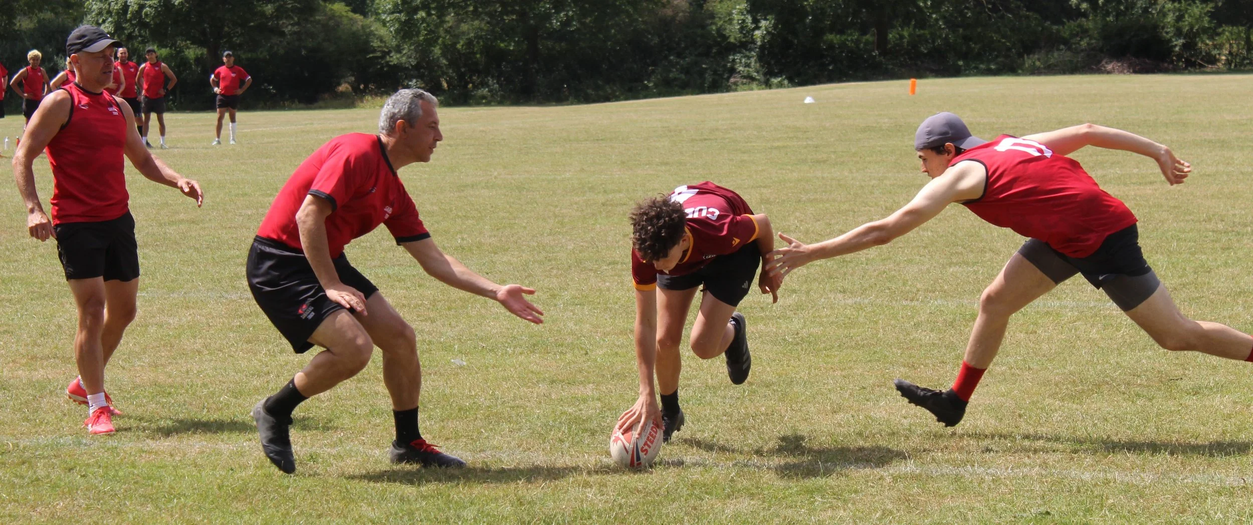 Rugby players and coach practicing a drill on a grassy field during daytime.