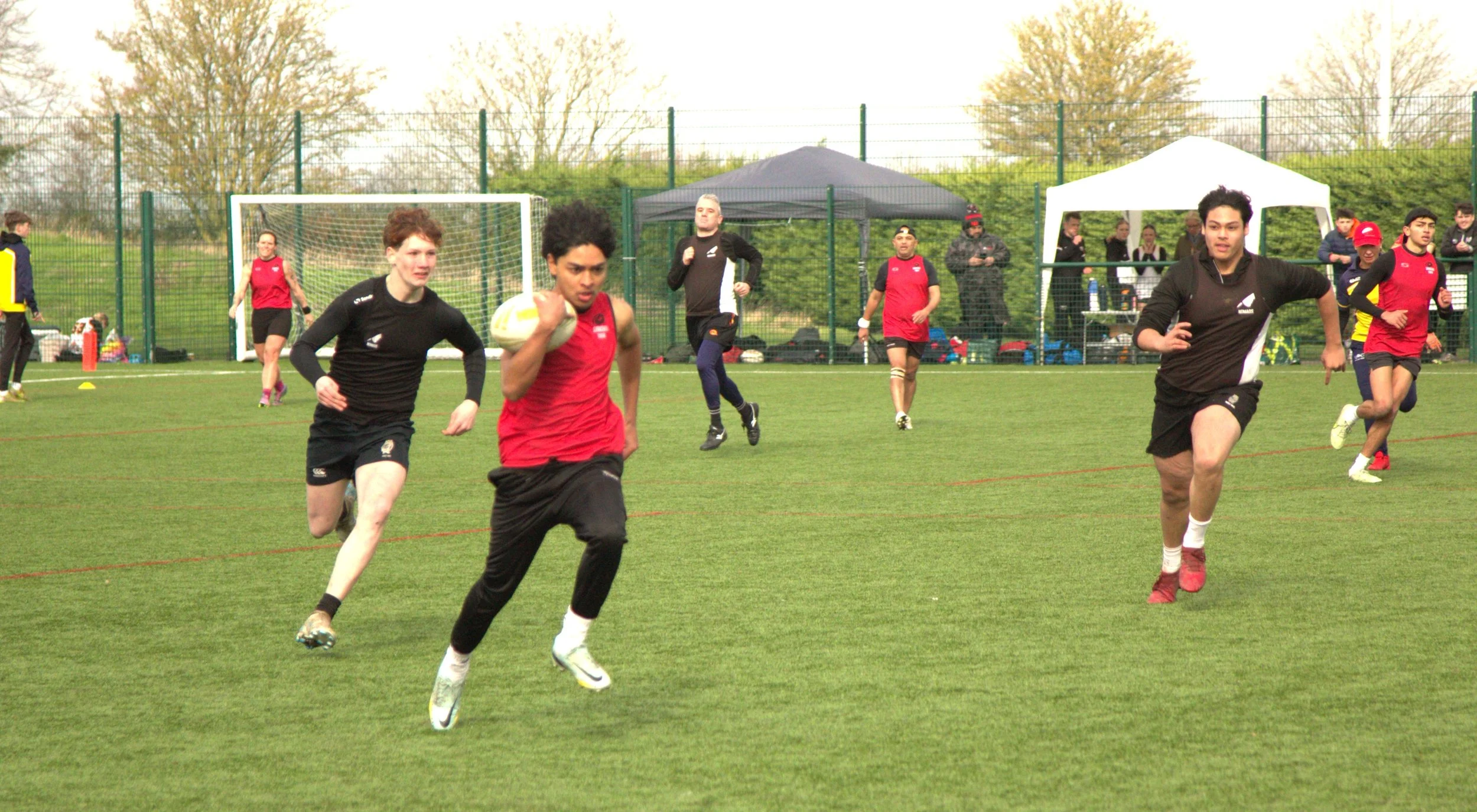Rugby players running during a match on a grassy field with a goalpost in the background.