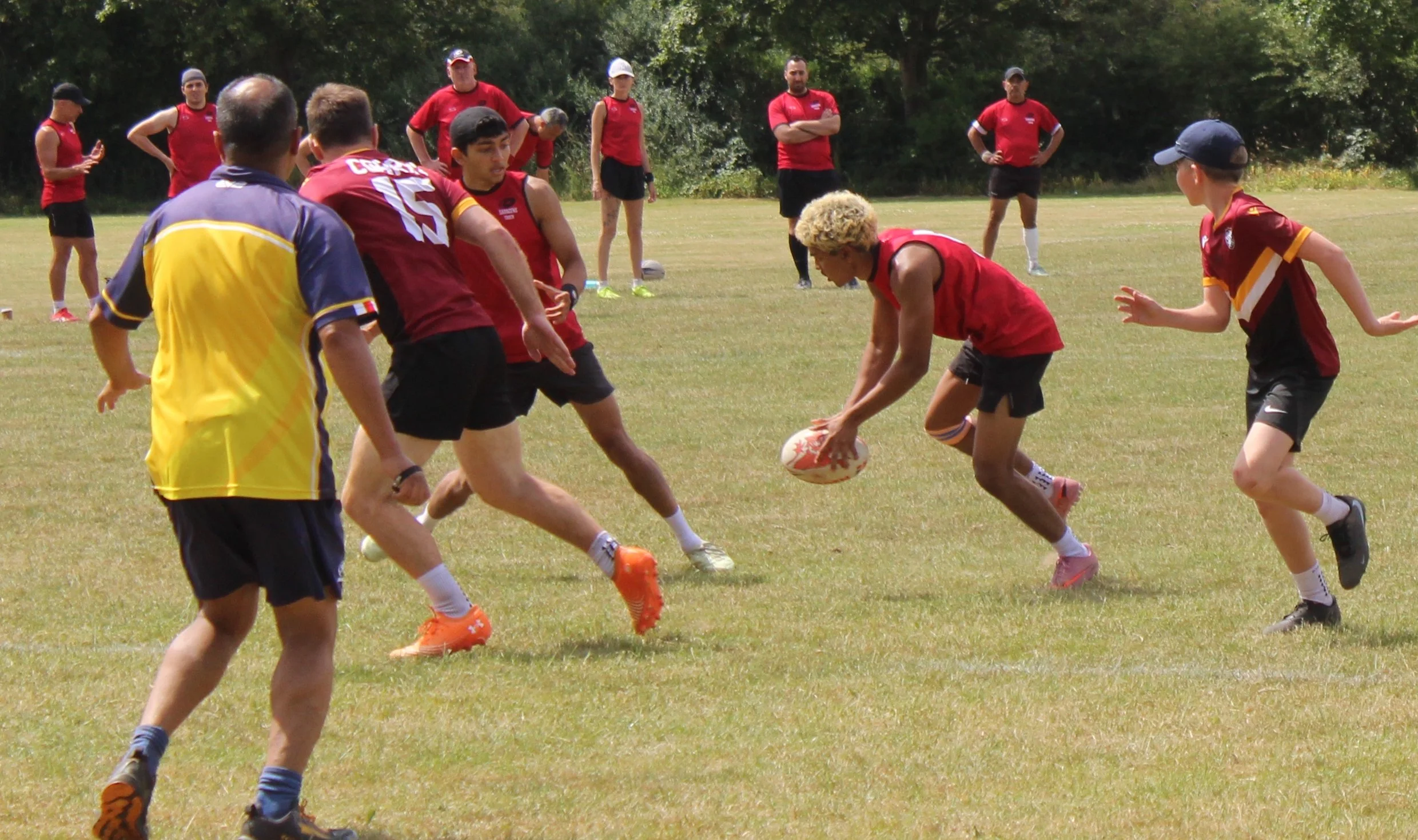 A group of people playing rugby on a grassy field surrounded by trees.