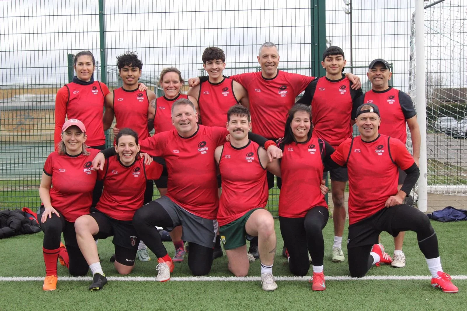 Group of people in red sports jerseys posing for a team photo at a sports field