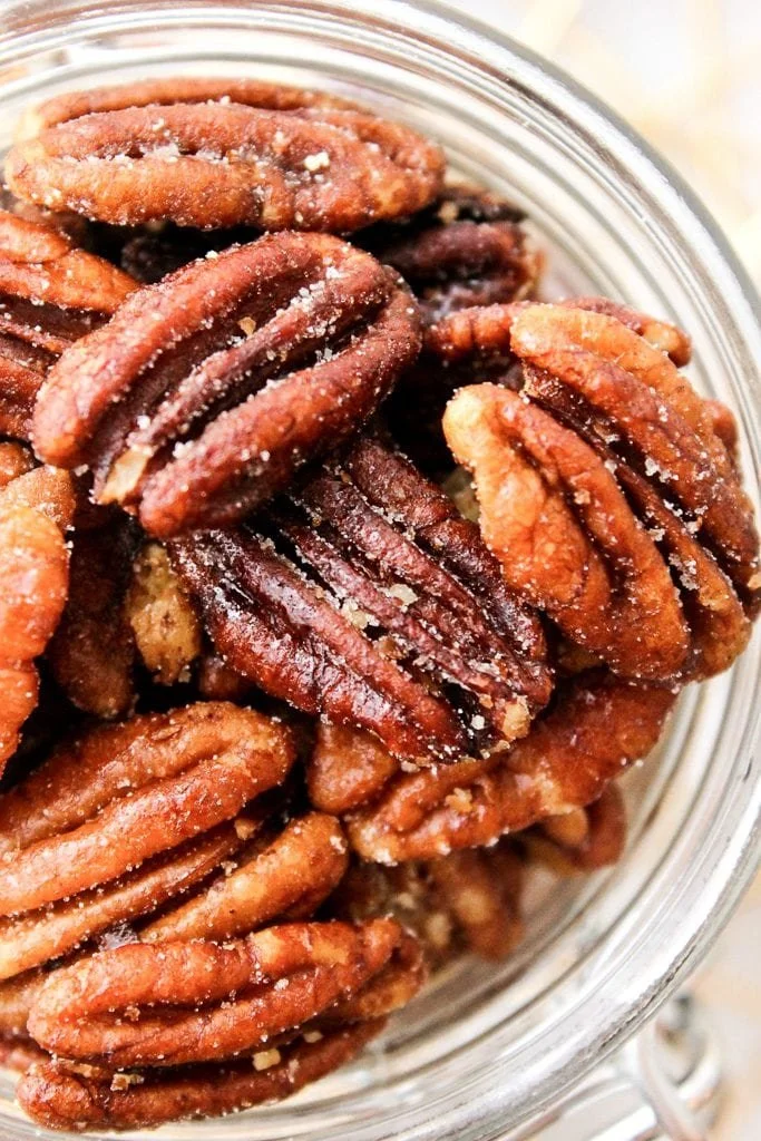 Close-up of roasted pecans in a glass jar with some salt crystals on the surface.