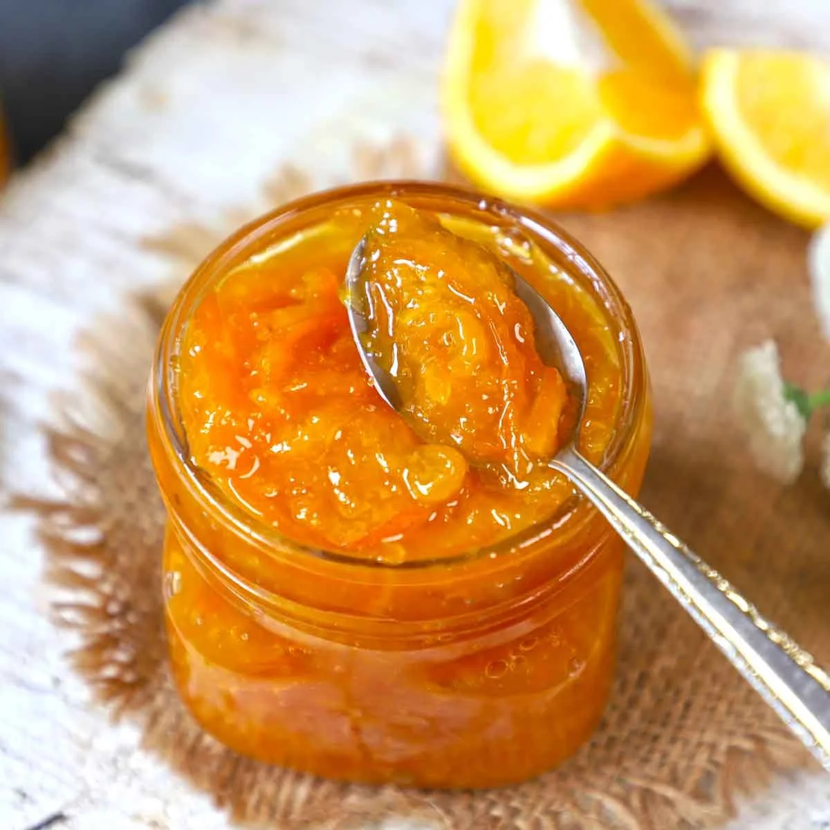 A jar of orange marmalade with a spoon inside it, with lemon wedges in the background.