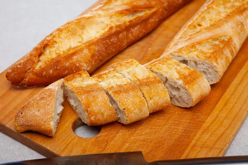 Slices of freshly baked baguette on a wooden cutting board.