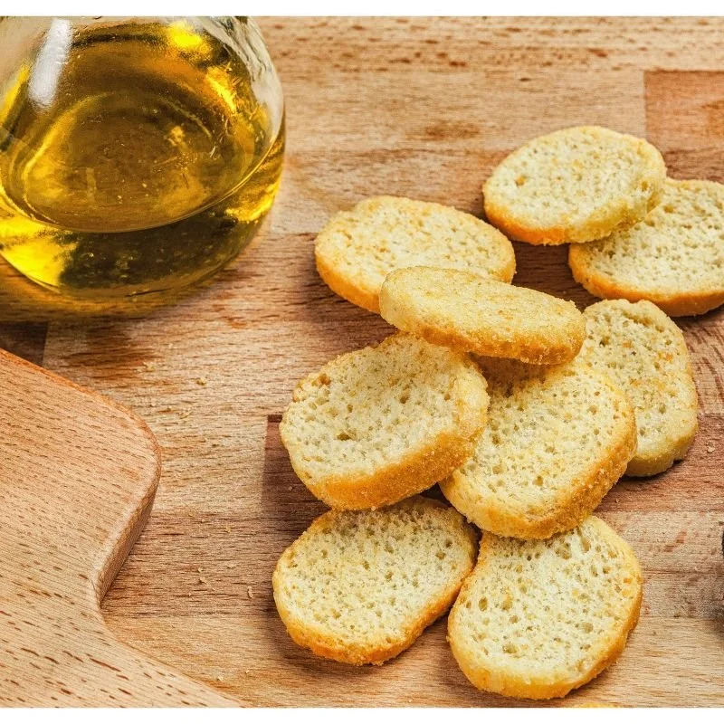 Bowl of olive oil and slices of toasted bread on a wooden cutting board.
