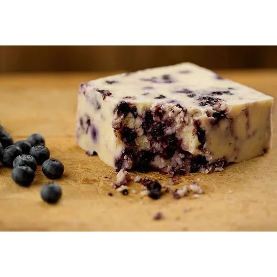A block of blueberry fudge on a wooden surface, with fresh blueberries scattered beside it.