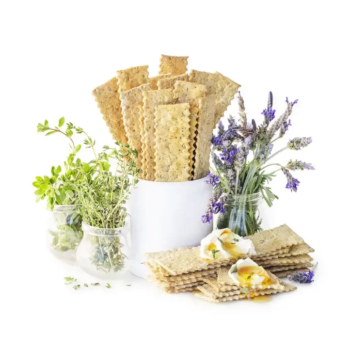 Stack of crispy flatbread surrounded by fresh herbs and lavender flowers on a white background.