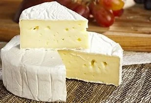 Two pieces of soft, white Brie cheese on a wooden surface.