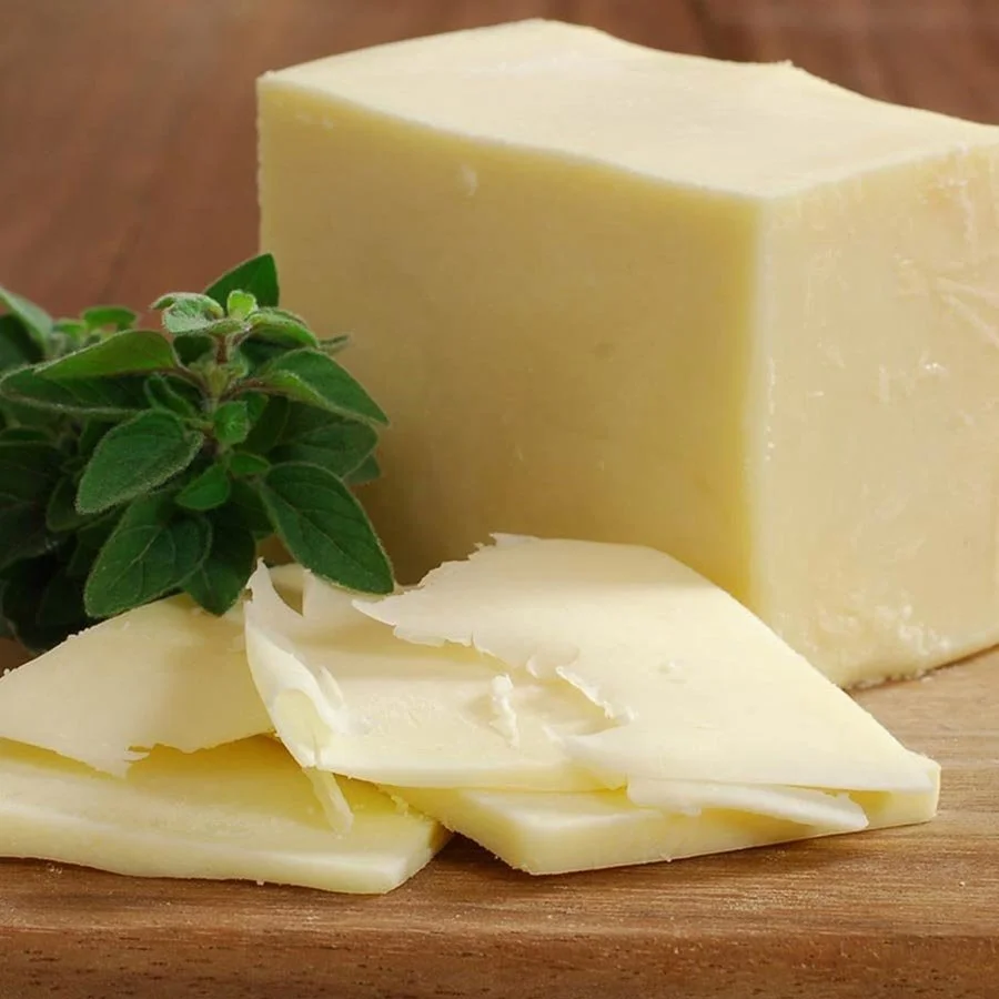 A block of shredded yellow cheese, sliced cheese, and fresh green herbs on a wooden surface.
