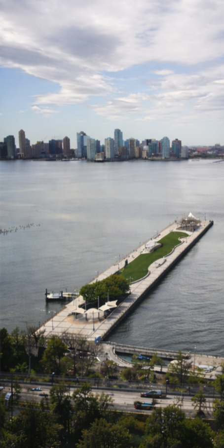 An aerial view of a city skyline across a river with a long park pier in the foreground.
