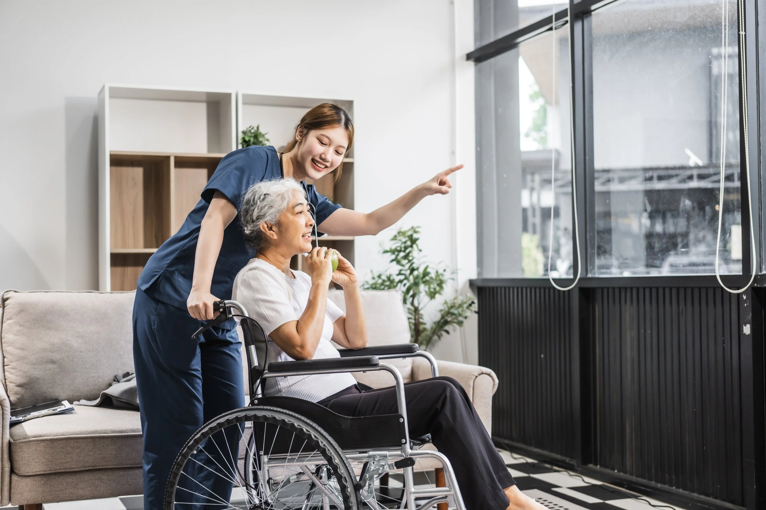 Caregiver assisting a senior woman in a wheelchair inside a retirement residence.