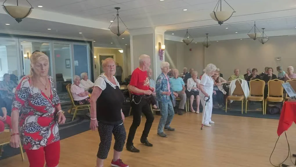 Des résidents dansent en ligne dans la salle d'activités de la Résidence Le Parc