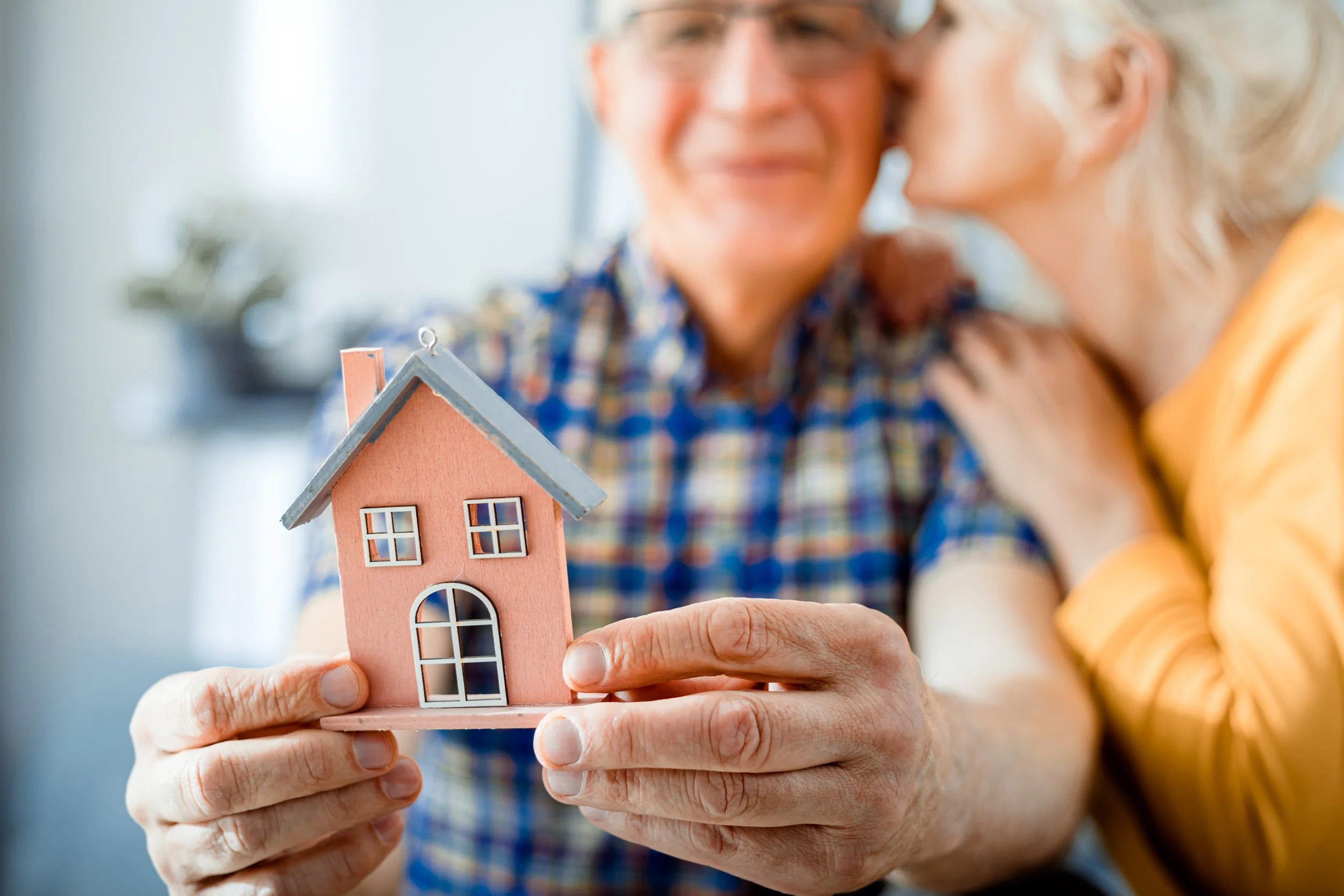 Senior couple holding a model house while planning their move to retirement living.