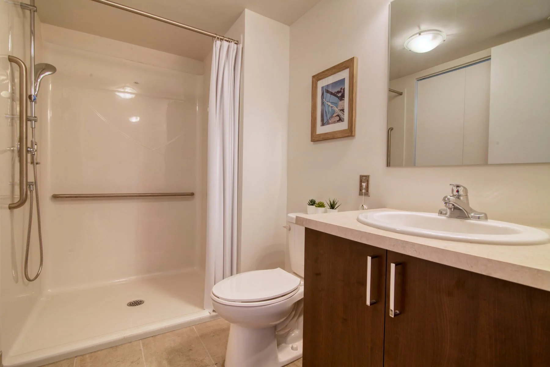 Salle de bain avec douche à l'italienne et barre d'appui dans un appartement témoin de la Résidence Le Parc