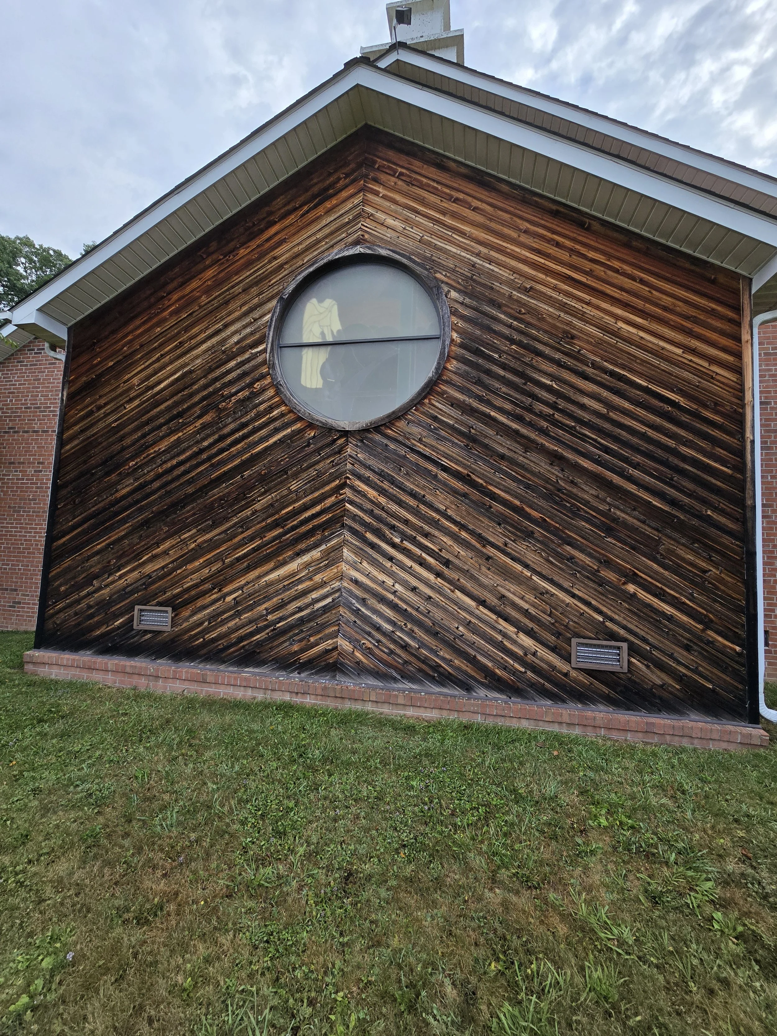 Front view of a house with a wood-paneled wall and a circular window, under a cloudy sky.
