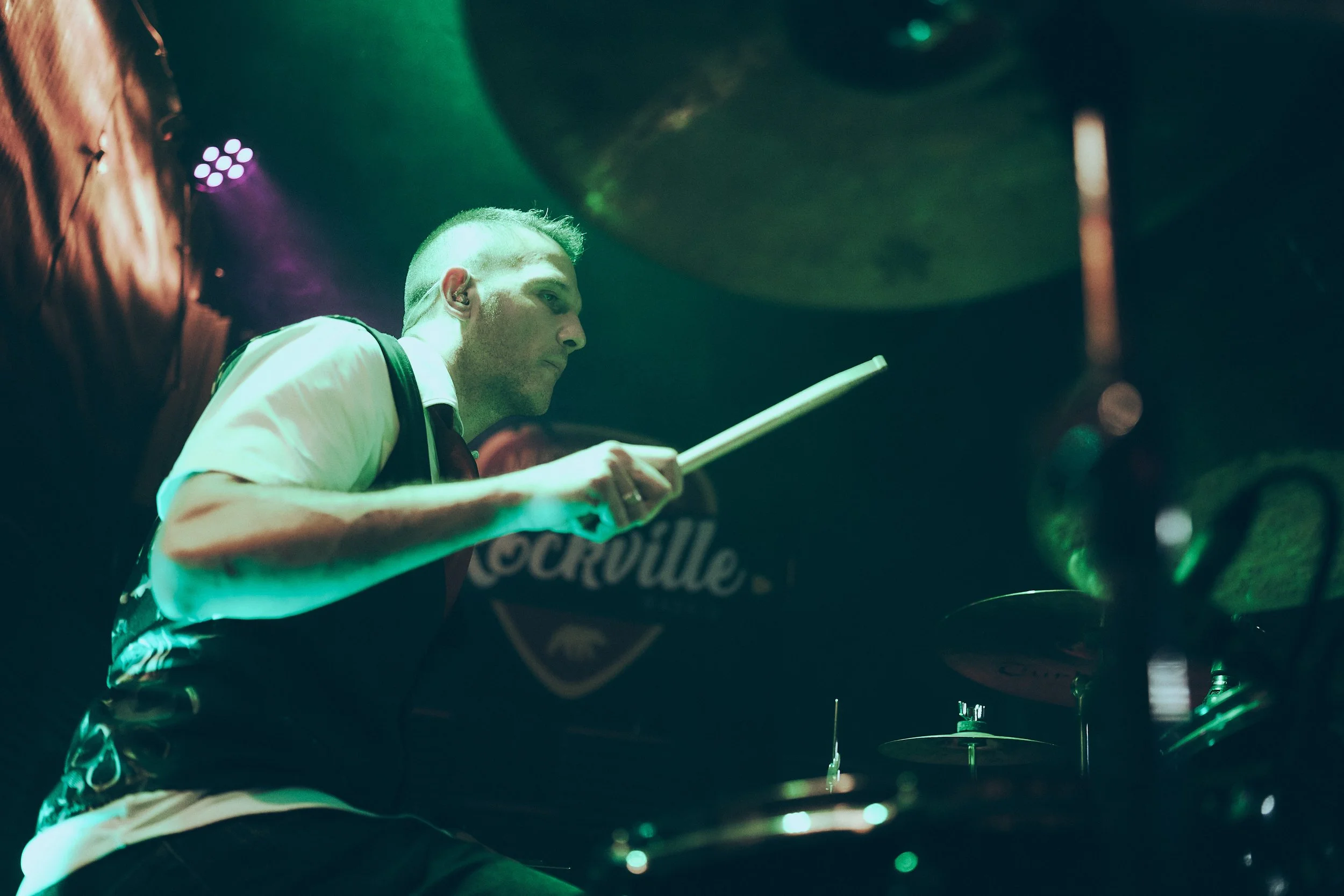 A male drummer playing drums on stage with colorful lighting.