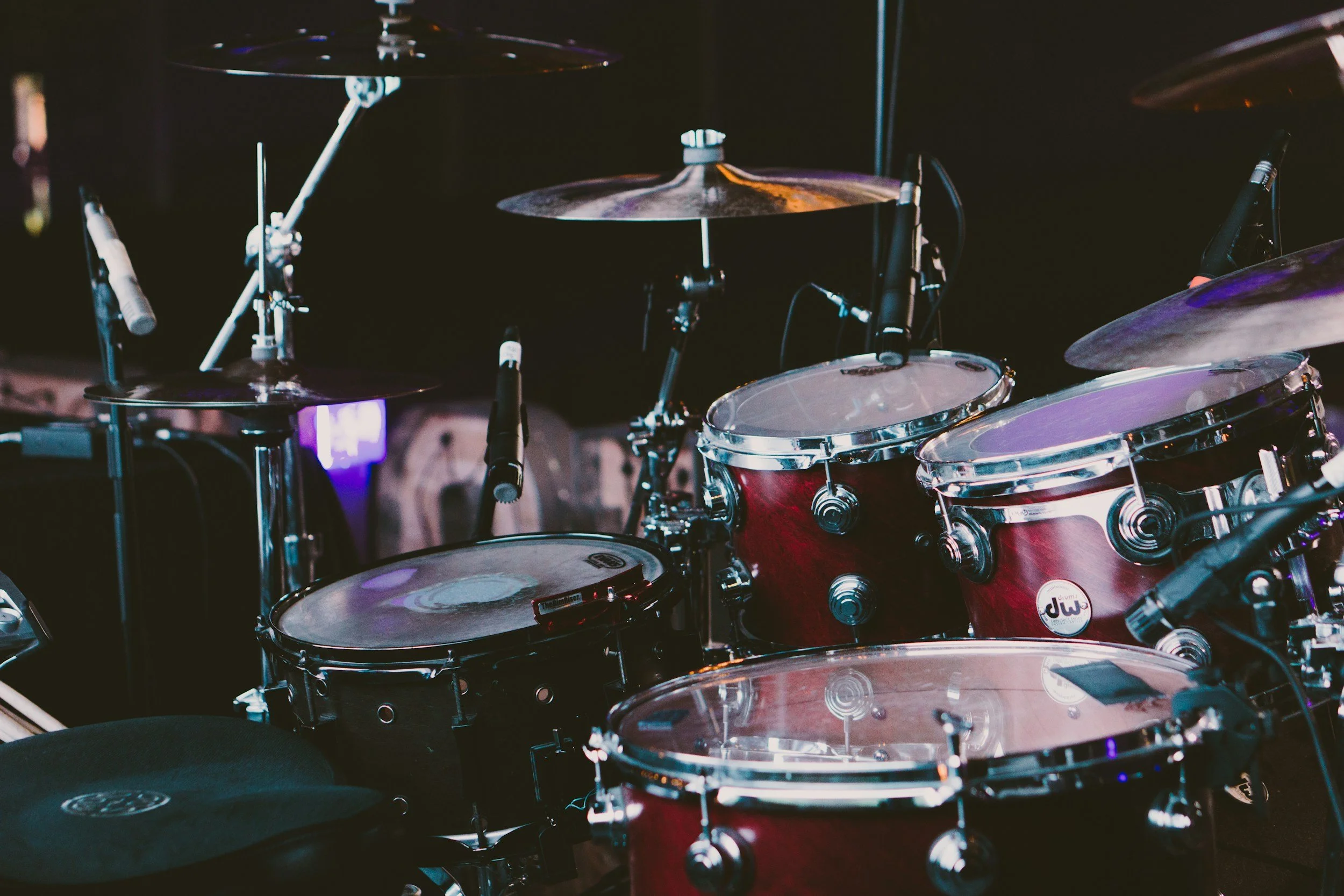 A set of red DW acoustic drums with cymbals and microphones on a stage, ready for a performance.
