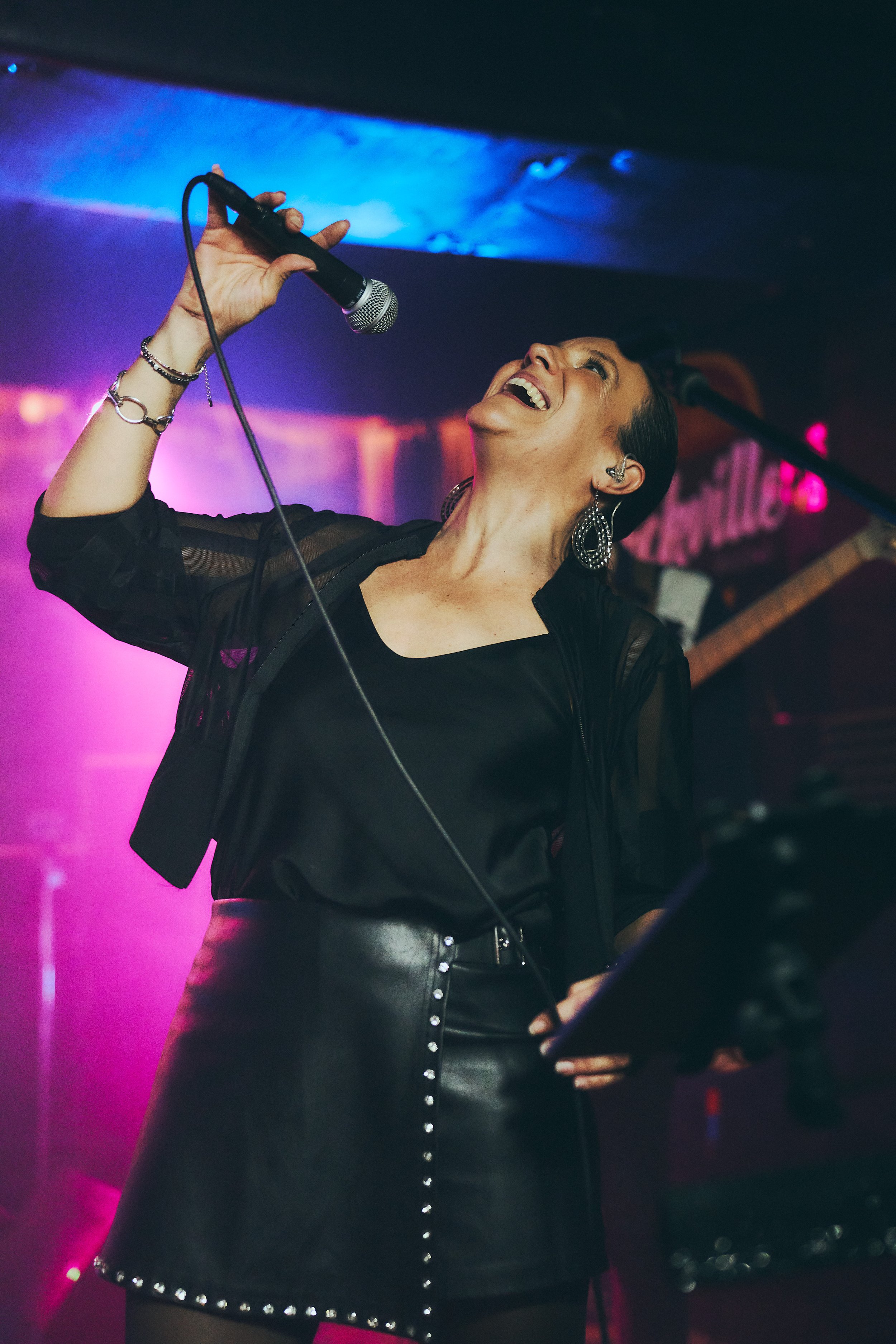 A woman singing into a microphone on stage with colorful lighting in the background.