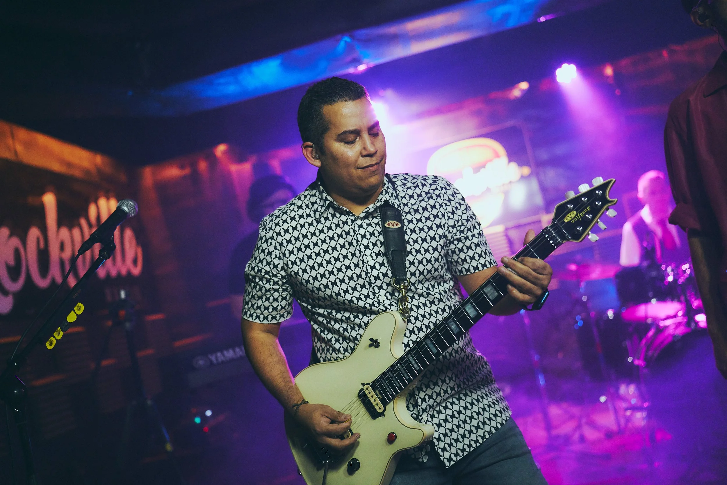 A man playing an electric guitar on stage at a live music event with colorful stage lights.