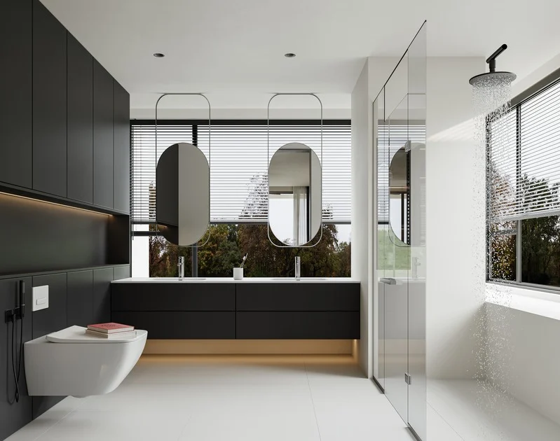 modern bathroom with black cabinetry, two oval mirrors, a double sink, a floating toilet, and a glass shower with rainfall showerhead, large windows with blinds showing trees outside