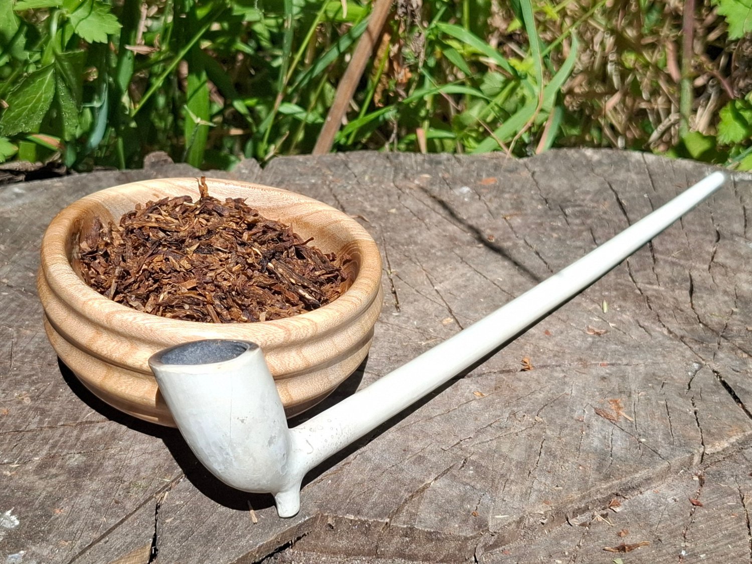 A wooden bowl filled with dried tobacco leaves placed on a tree stump outdoors.