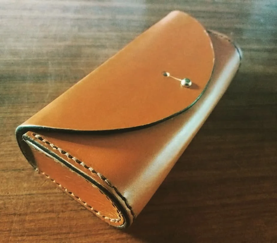 A leather wallet with a fold-over flap and a metal pin closure, placed on a wooden surface.