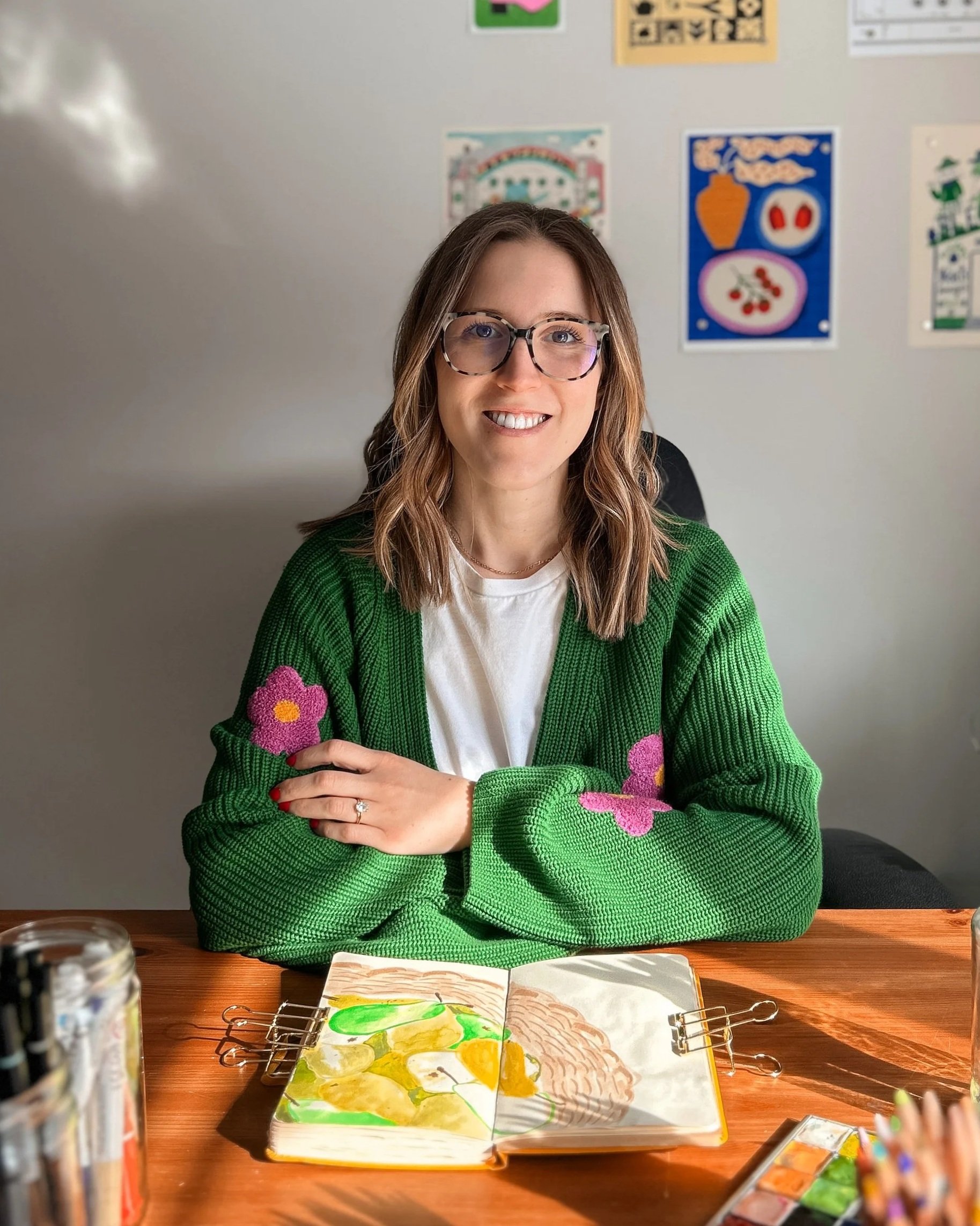 Samantha Curotte at her desk with open sketchbook featuring a mixed media pear illustration.
