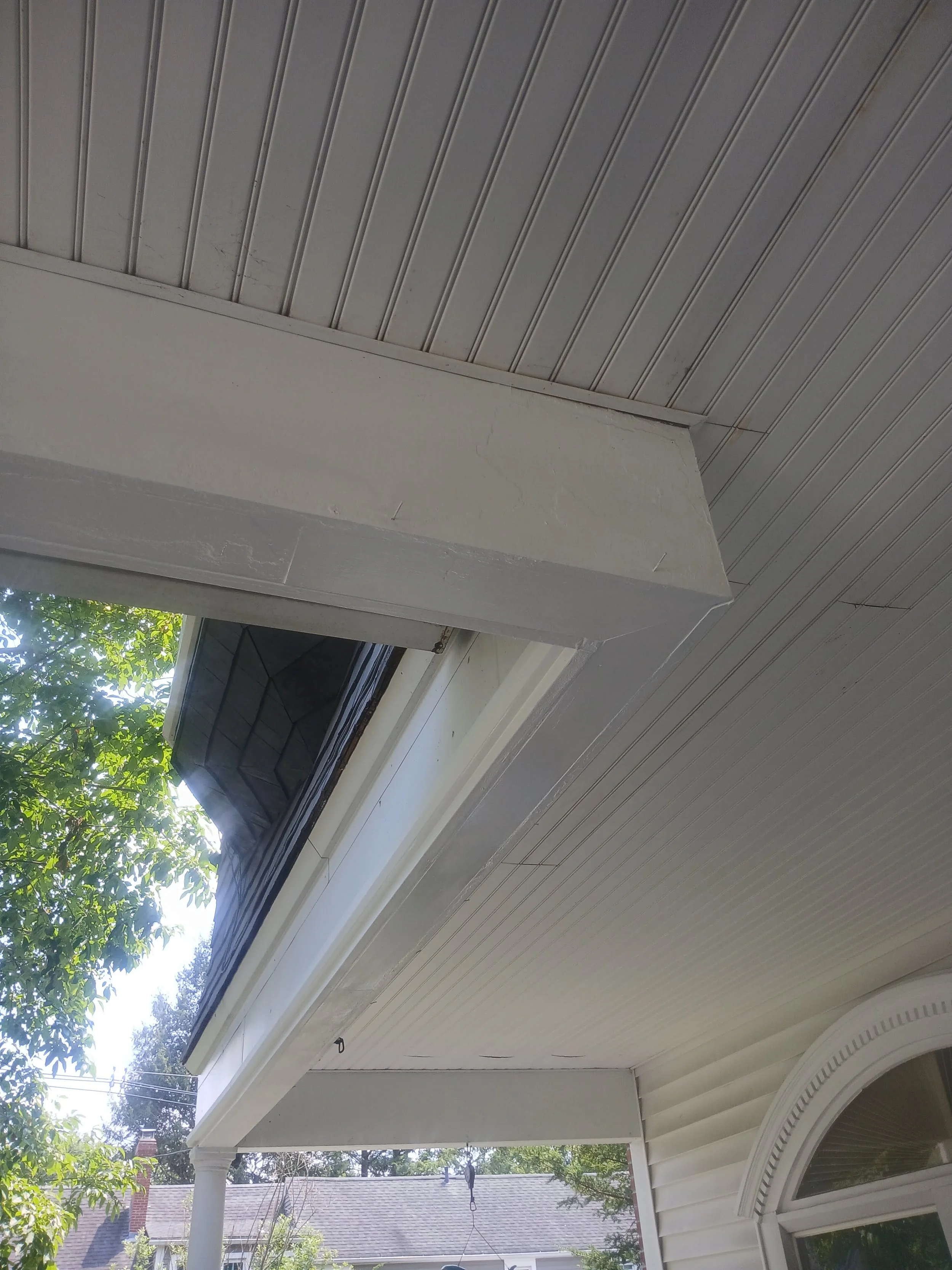 View of house exterior with a window, part of the roof, trees, and neighboring houses visible outside.