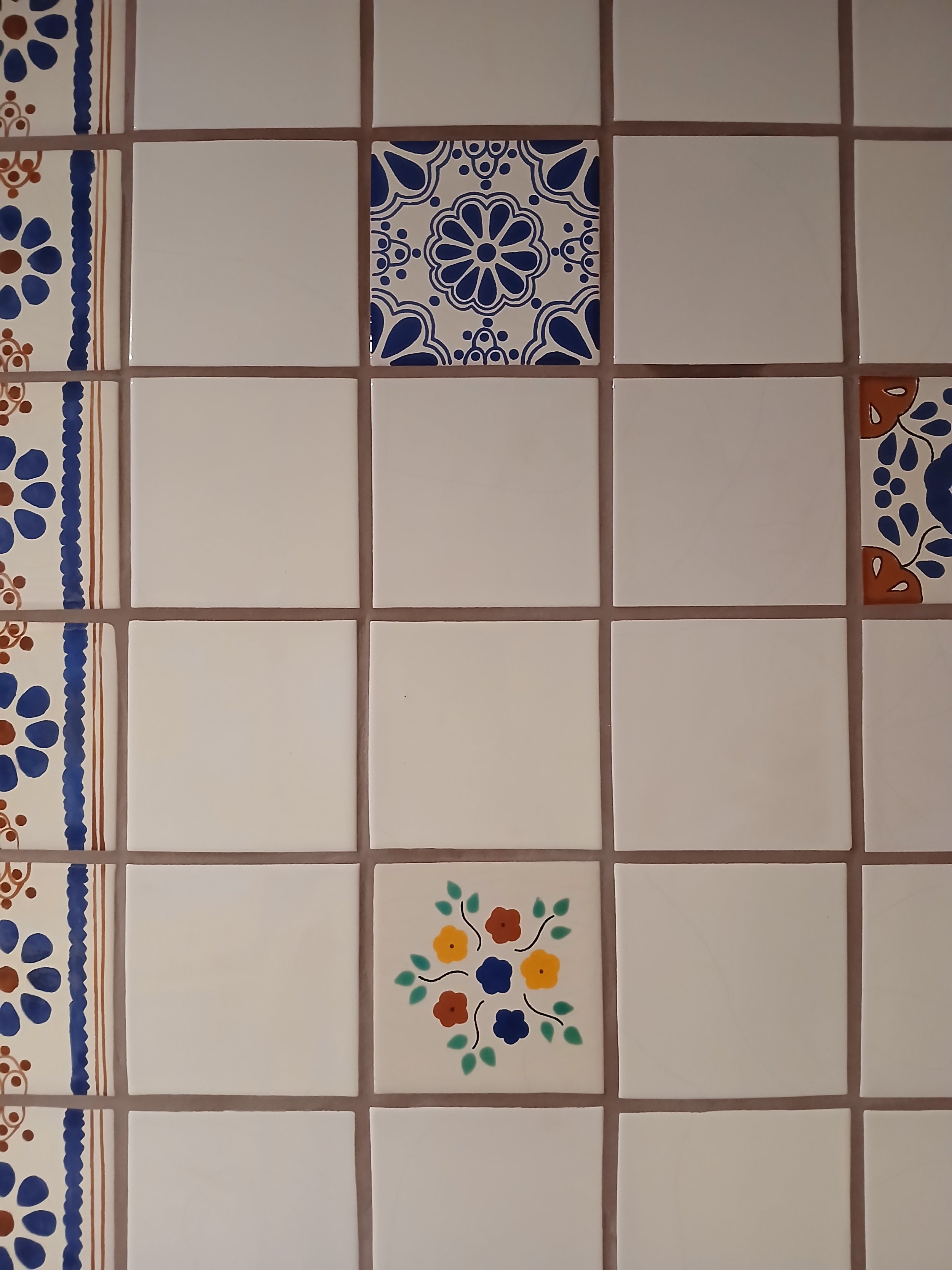 A tiled wall with various decorative ceramic tiles, including a blue and white floral pattern, a floral medallion, and geometric designs in yellow, green, and red.